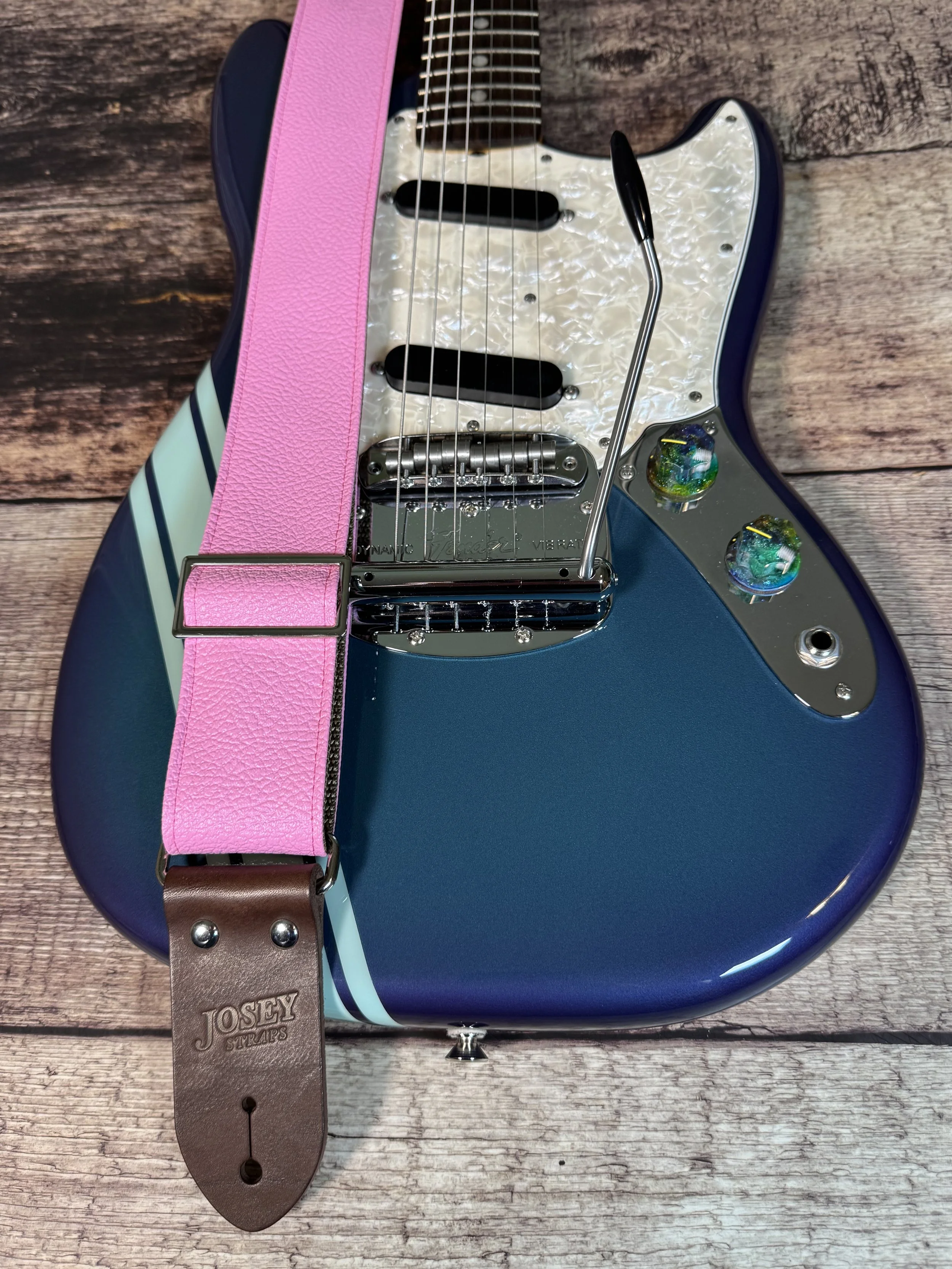 Bubblegum pink tolex guitar strap on wooden floor with guitar.
