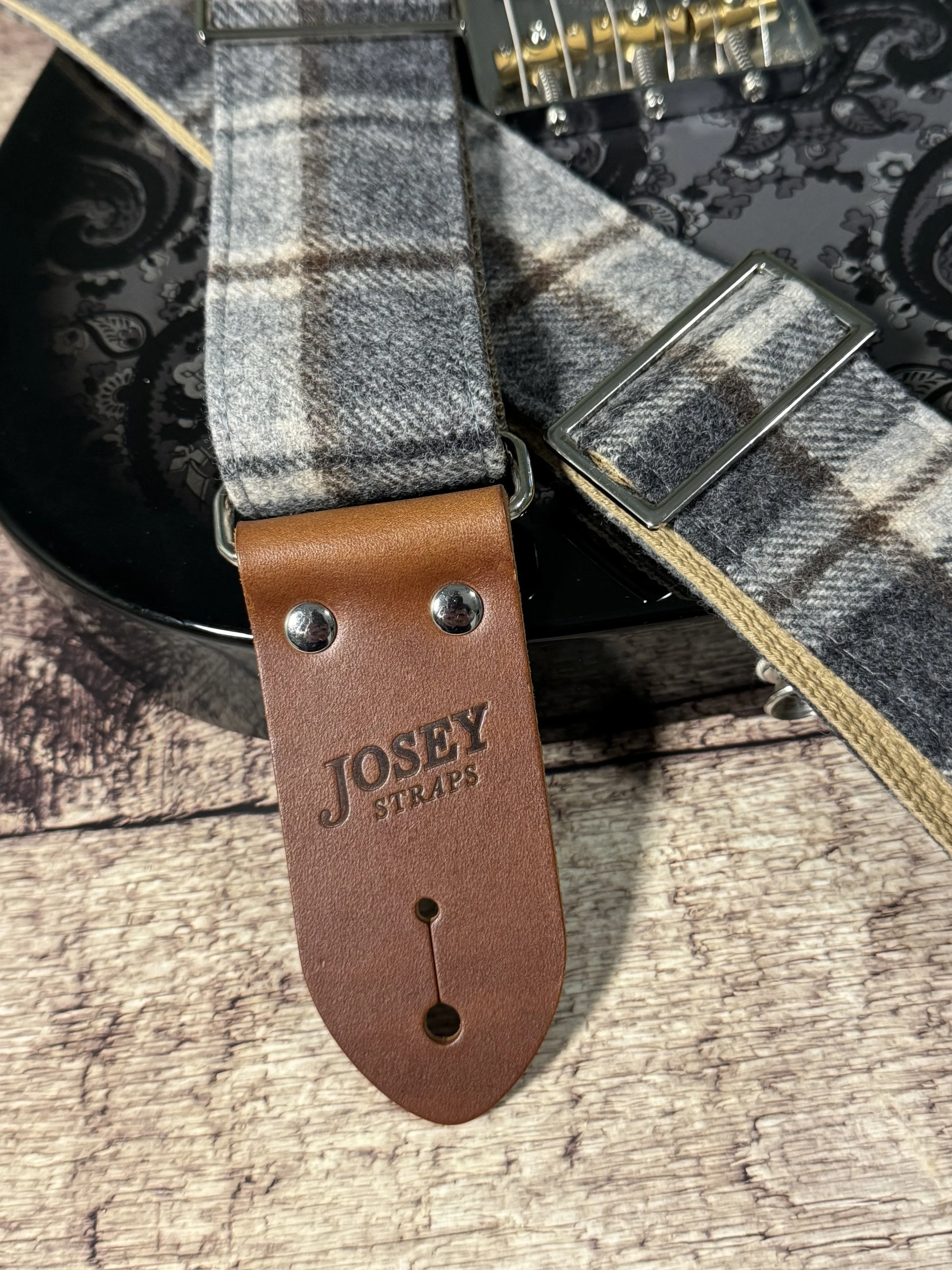 Vintage style grey plaid guitar straps on black guitar.