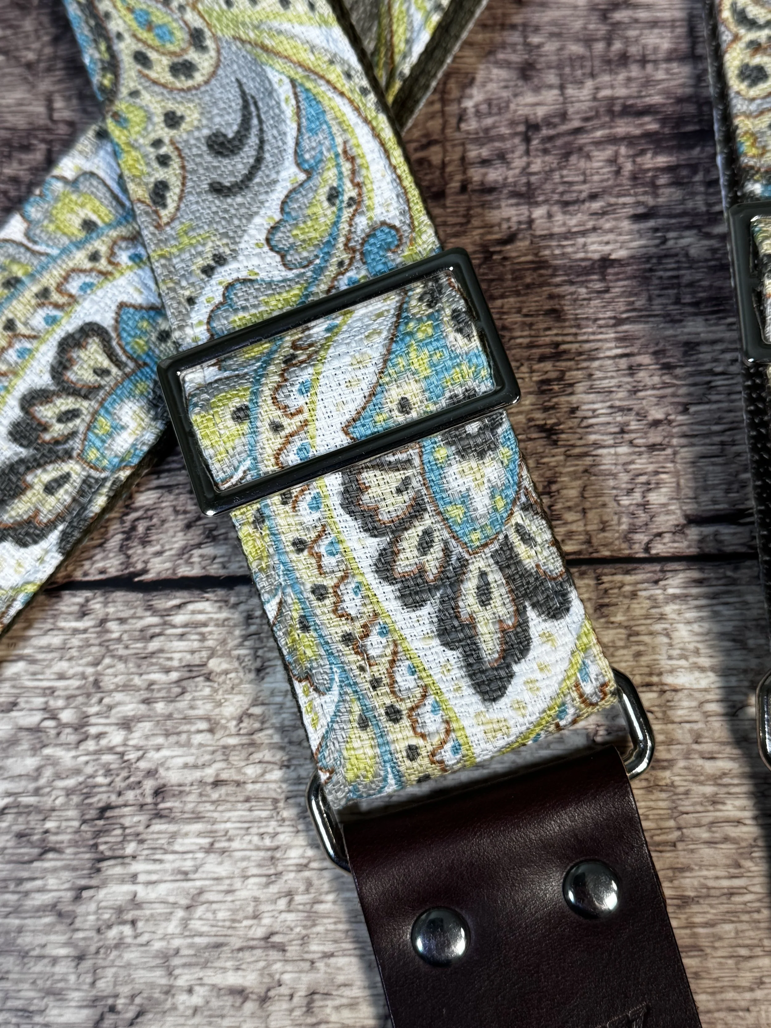 Graisley handmade paisley guitar strap featuring a gray, cream, blue, and mustard vintage-inspired pattern with premium leather ends.