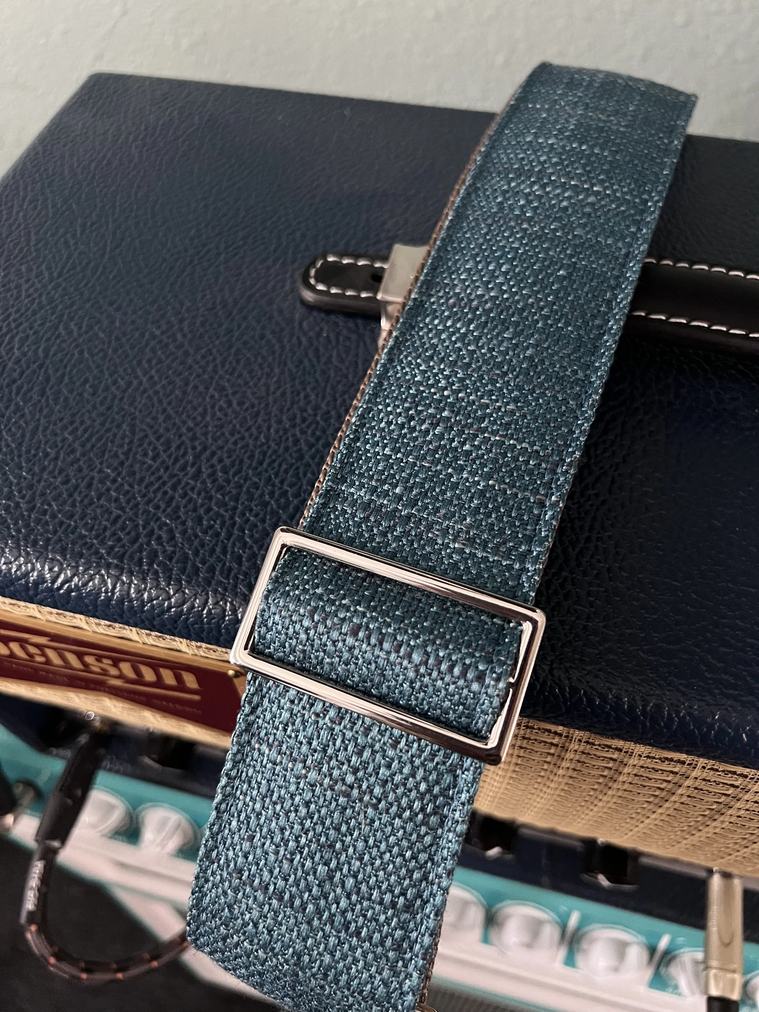 Peacock Blue woven guitar strap with blue-green texture and leather ends by Josey Straps resting on a guitar amp.