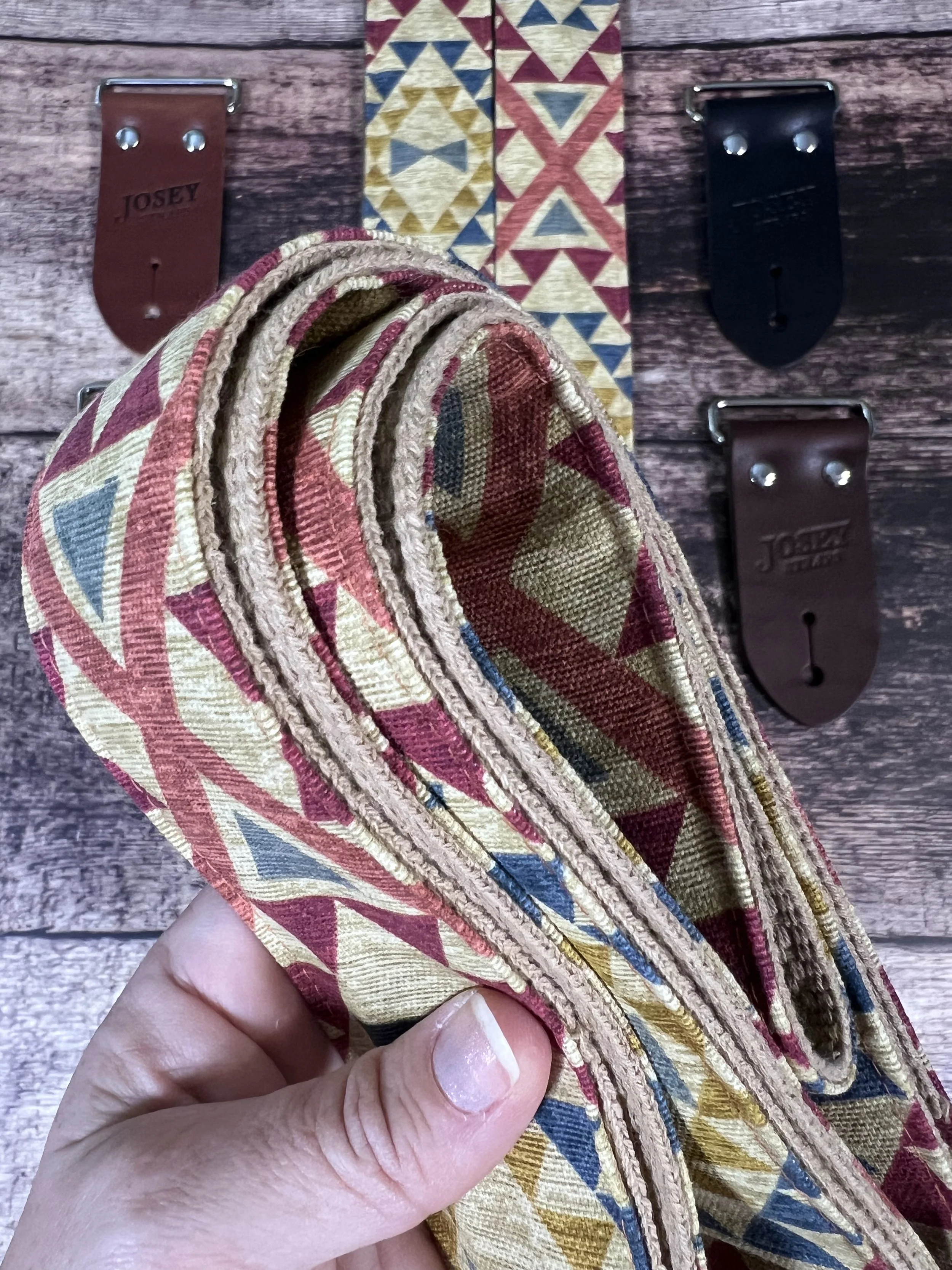 up close rolled up guitar strap showing grain detail of the fabric and backing. background of leather end choices on wood backdrop