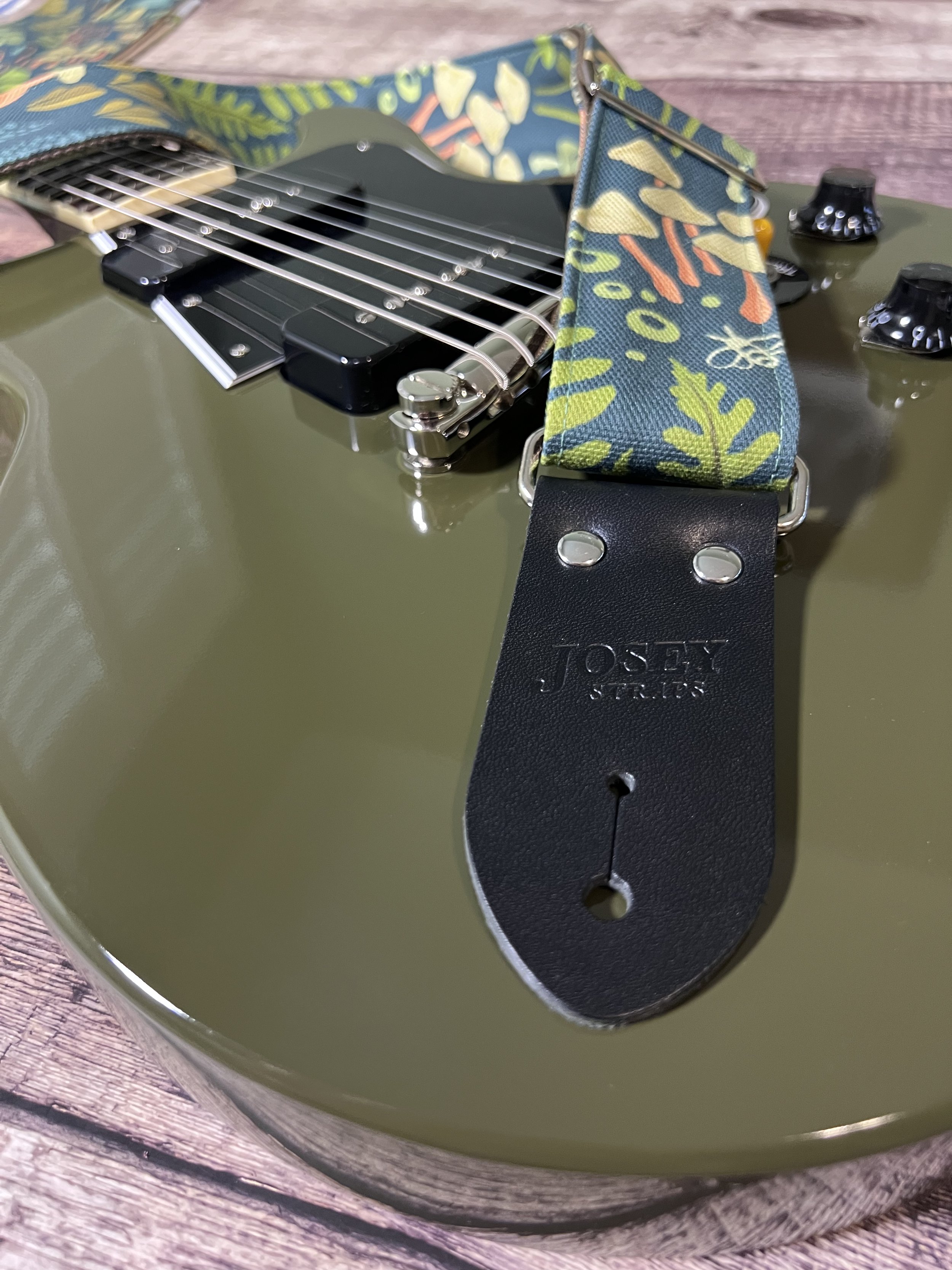 Dark botanical guitar straps on olive green guitar.
