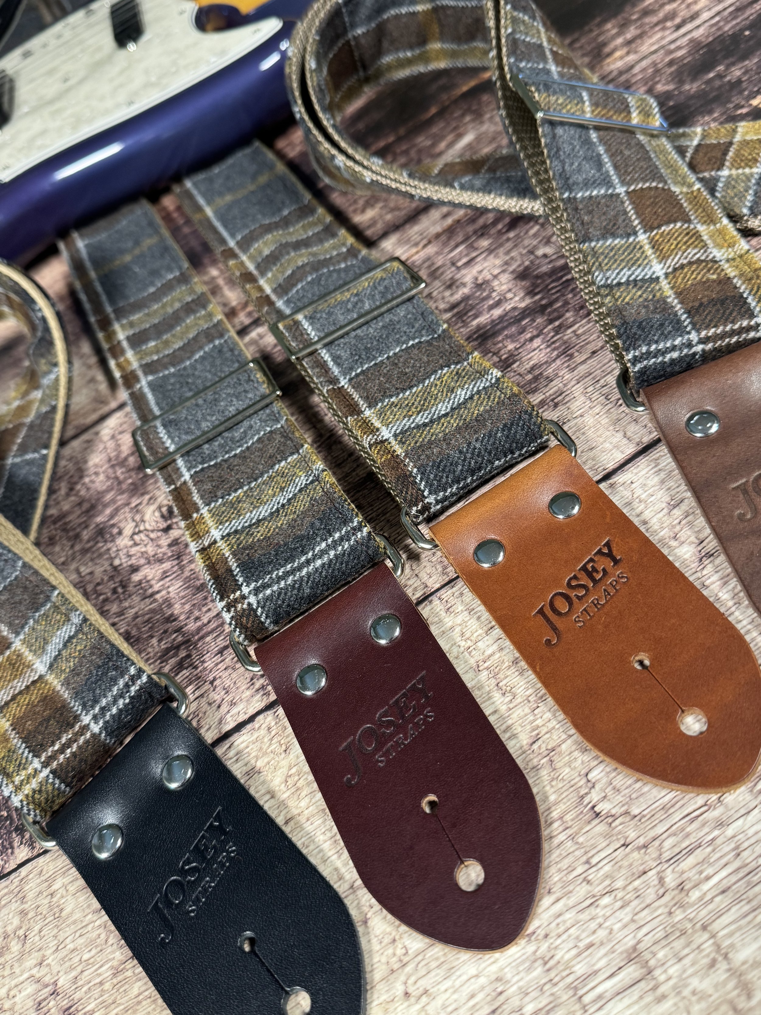 Ashes plaid guitar strap with leather ends by Josey Straps displayed on wood background