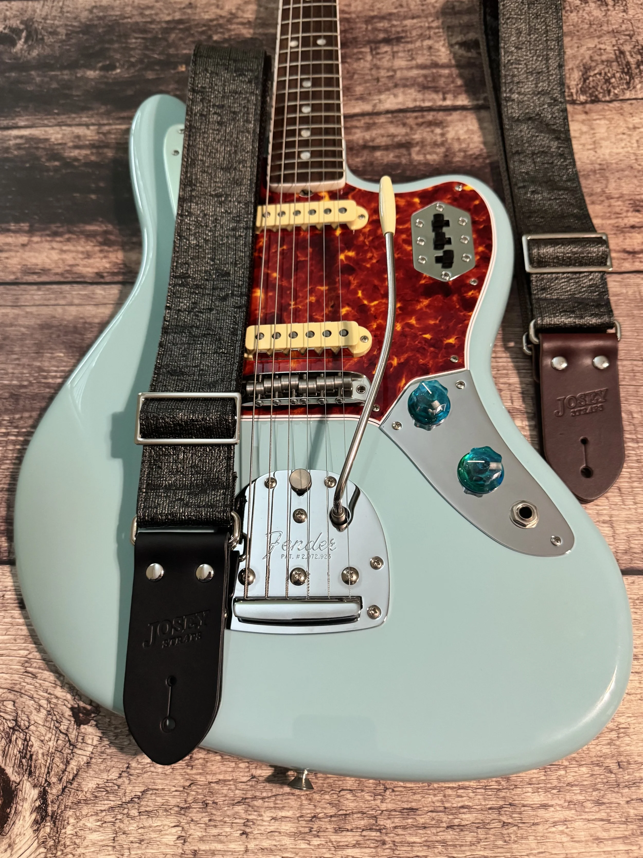 Pewter Slub guitar straps on on top of and next to a blue guitar.