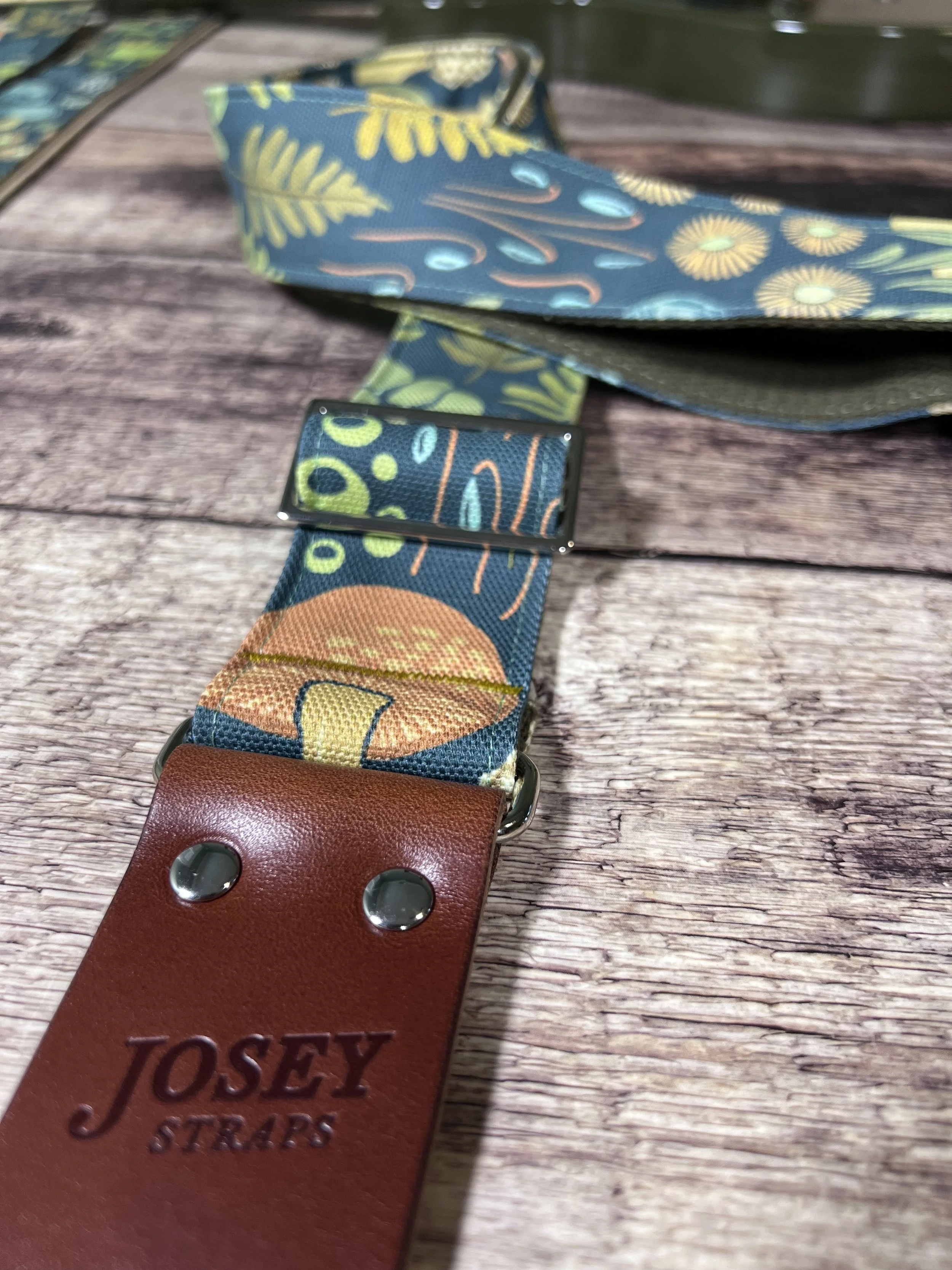 Dark botanical guitar straps on wooden backdrop.