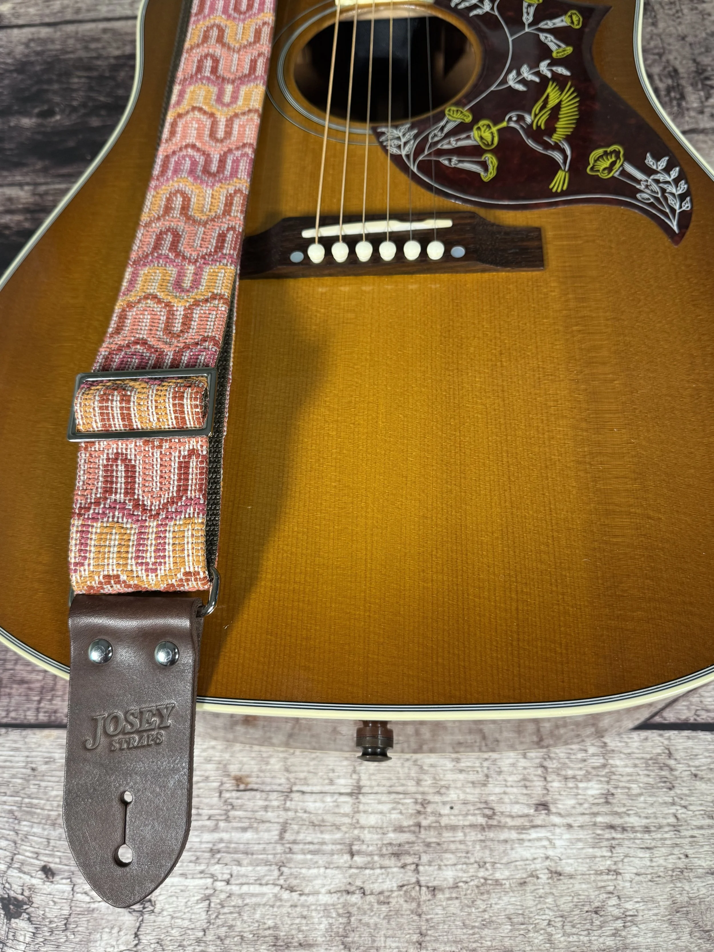 Vintage disco-inspired woven guitar strap in terracotta and gold tones by Josey Straps.  These strap is set on an acoustic guitar.