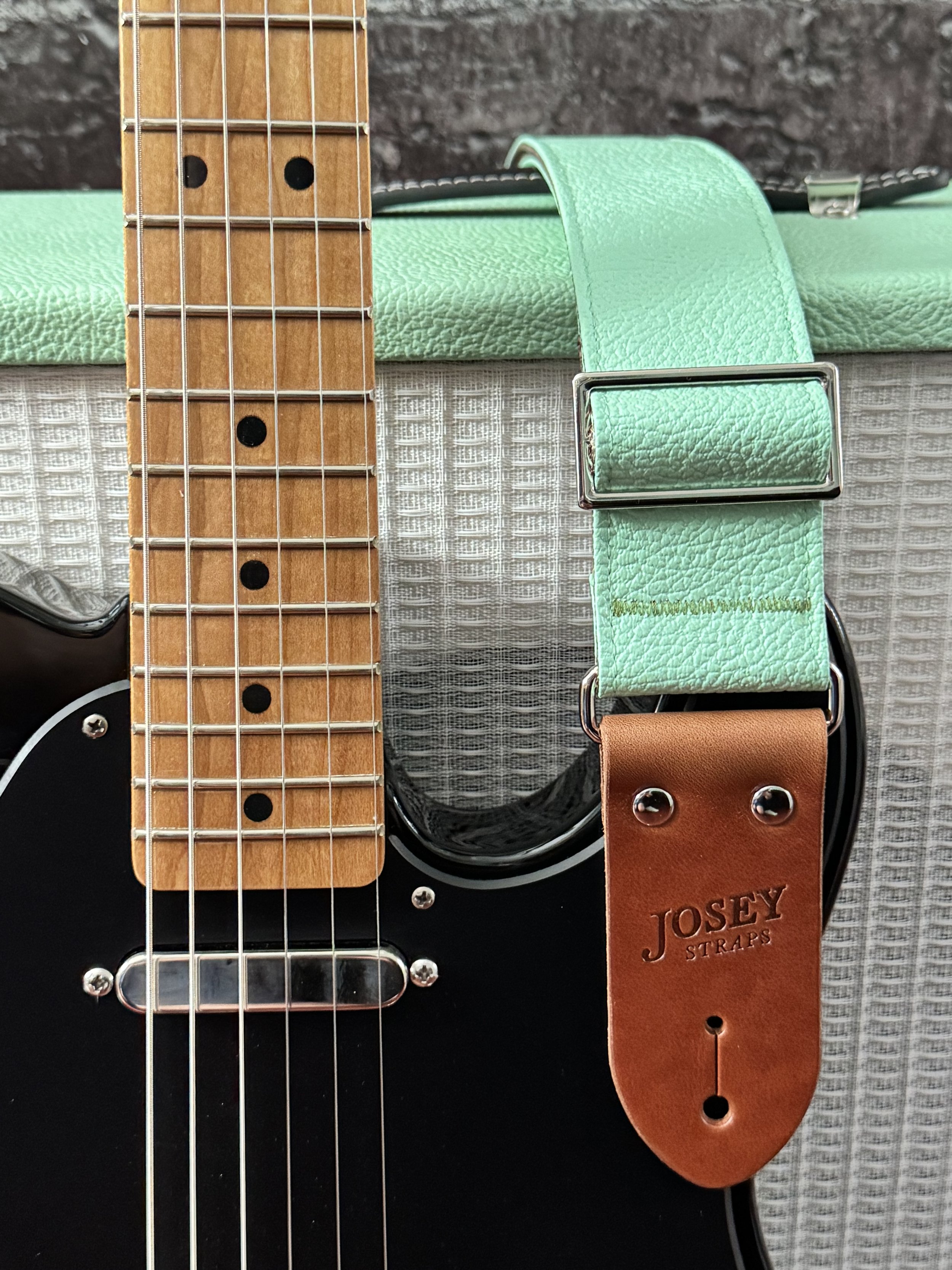 Seafoam green guitar strap draped over a guitar amplifier and black guitar.