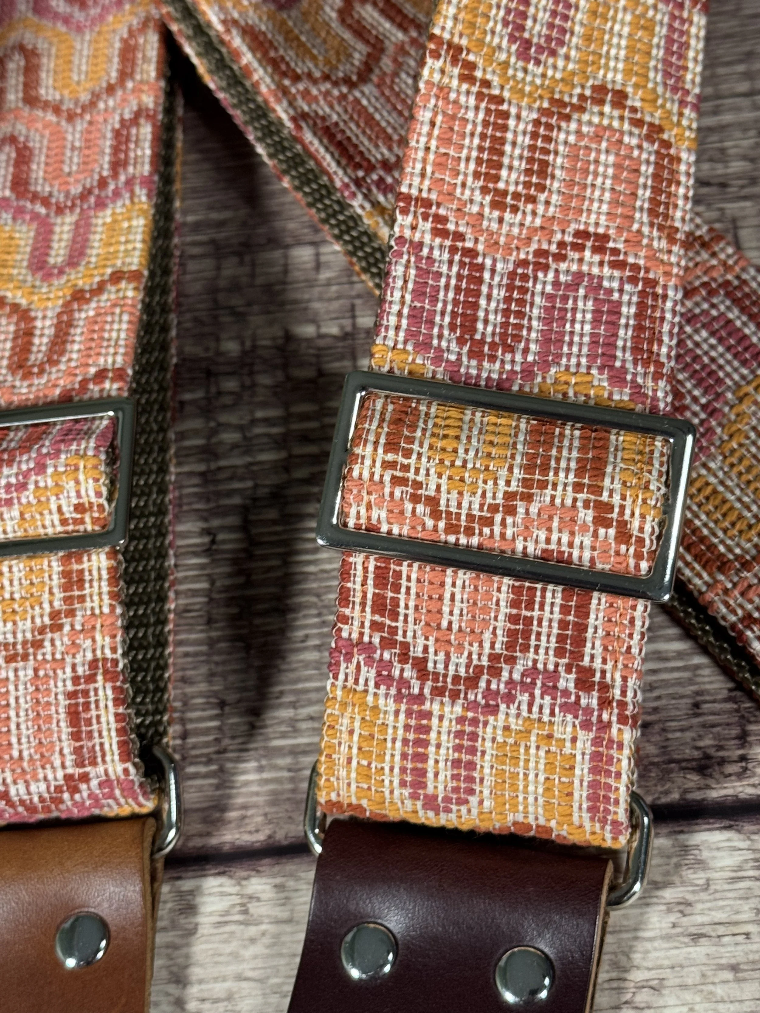 Vintage disco-inspired woven guitar straps in terracotta and gold tones by Josey Straps.  These straps are set on wood backdrop.