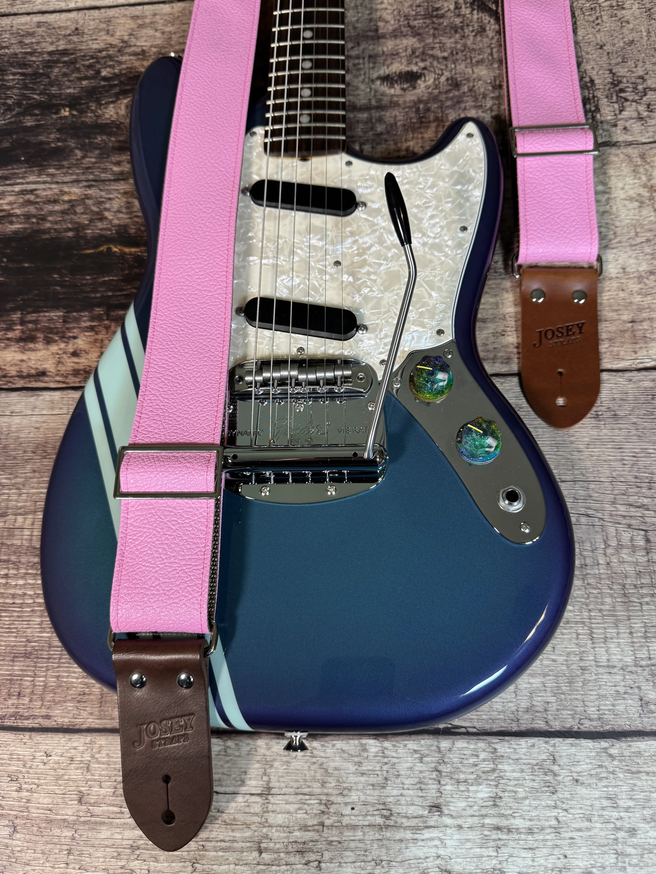 Bubblegum pink tolex guitar straps on wooden floor with guitar.