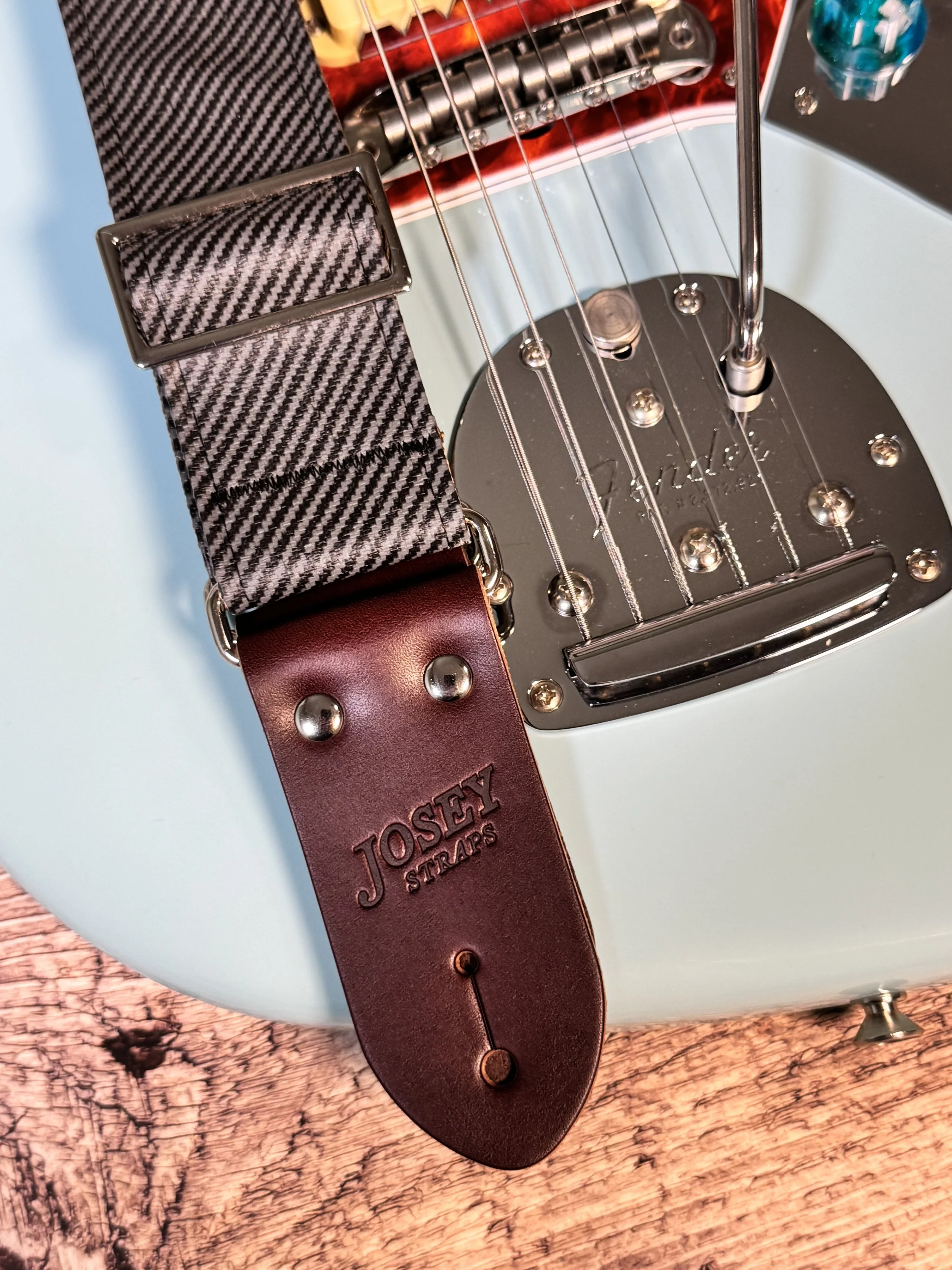 Close up shot of charcoal tweed guitar strap on blue guitar.