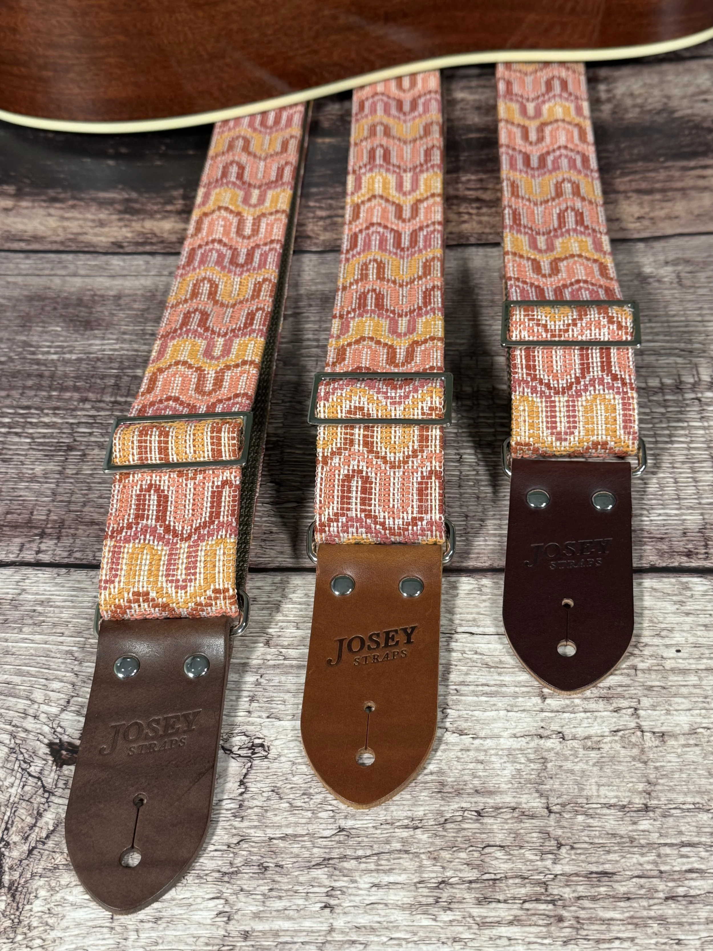 Vintage disco-inspired woven guitar straps in terracotta and gold tones by Josey Straps.  These straps are set on wood backdrop.