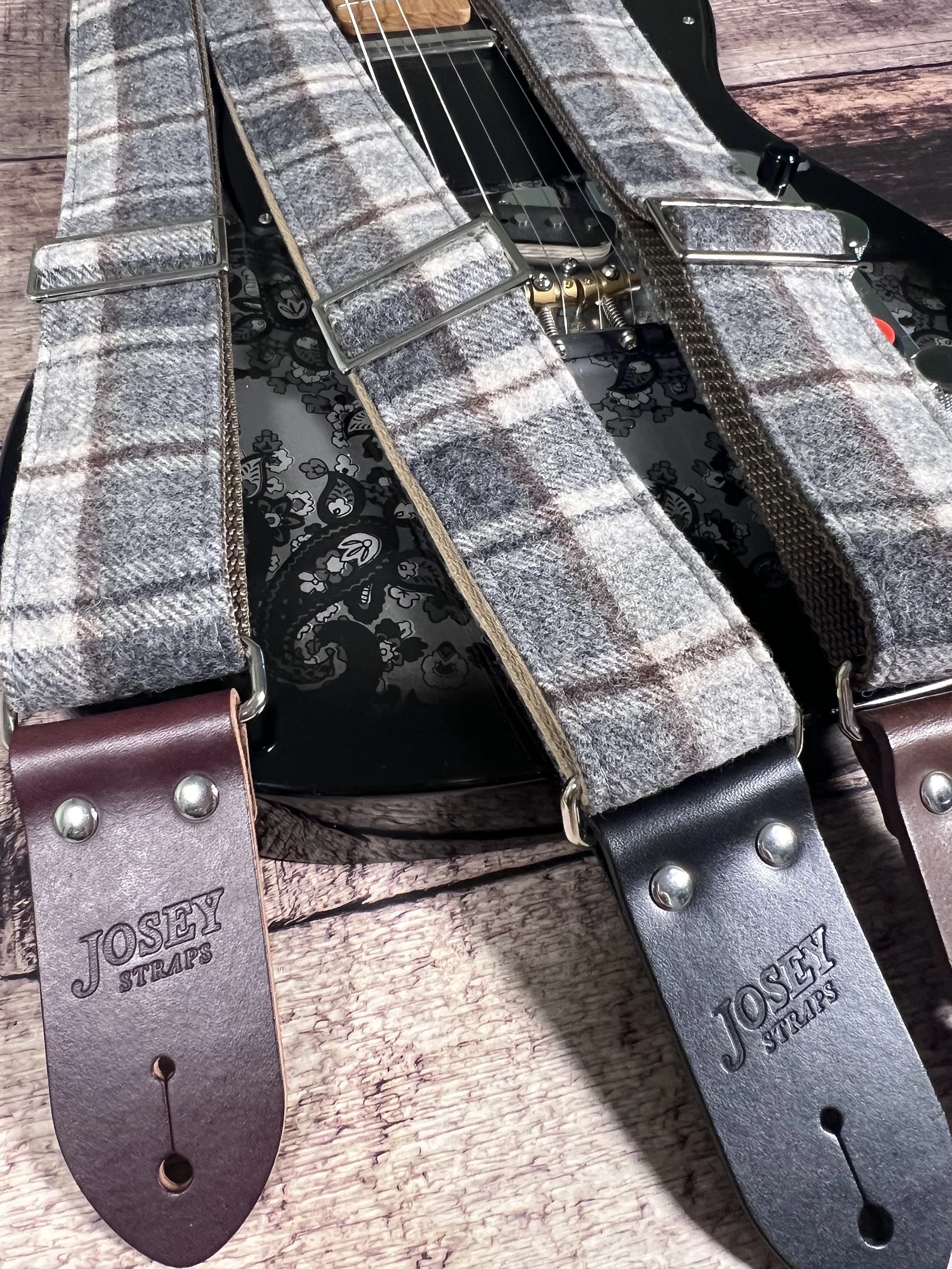 Vintage style grey plaid guitar straps on black guitar.