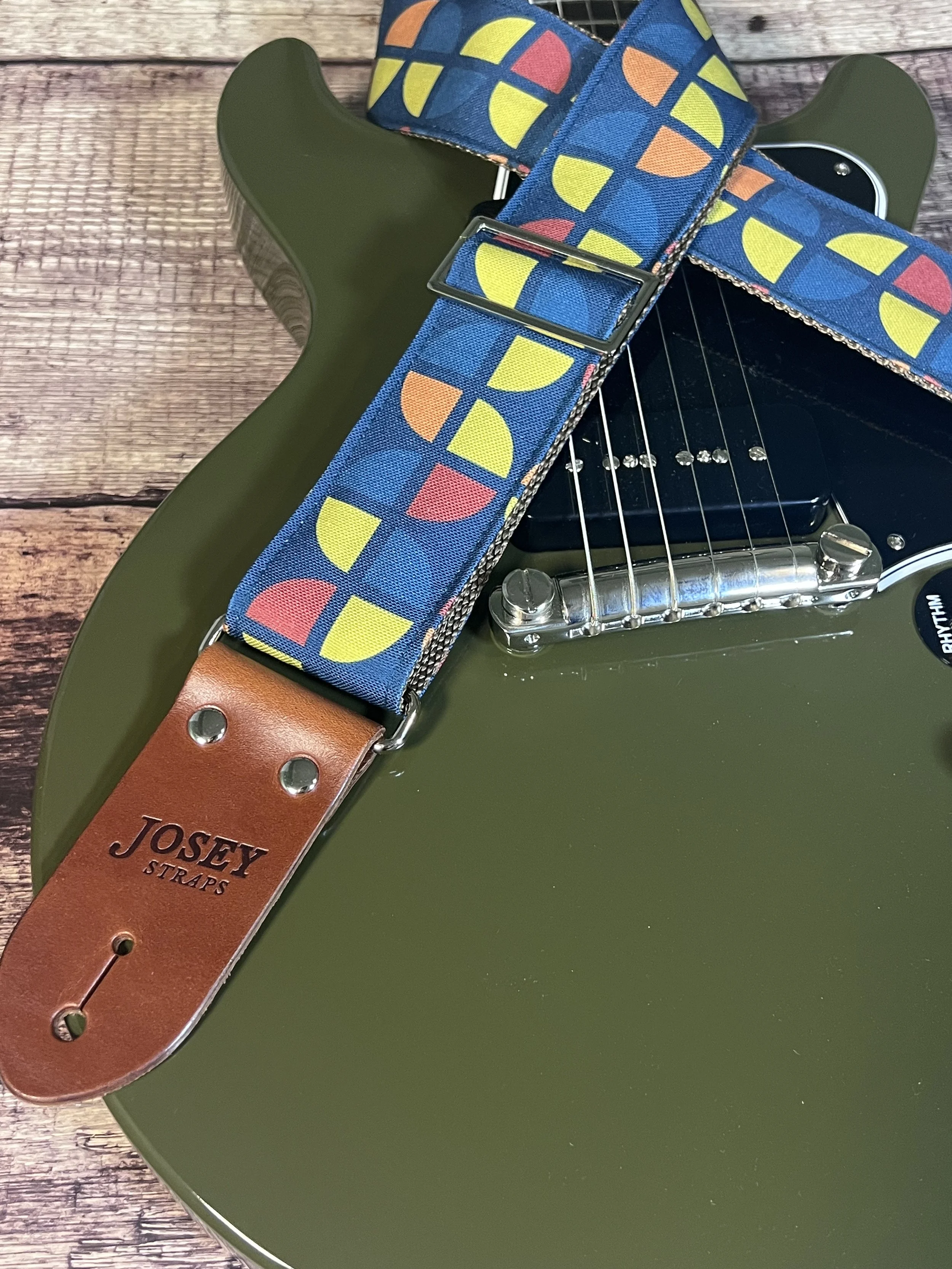 Navy blue guitar straps with groovy goemetric circle pattern in mustard yellow, coral, and steel blue, laid flat on an olive green colored electric guitar