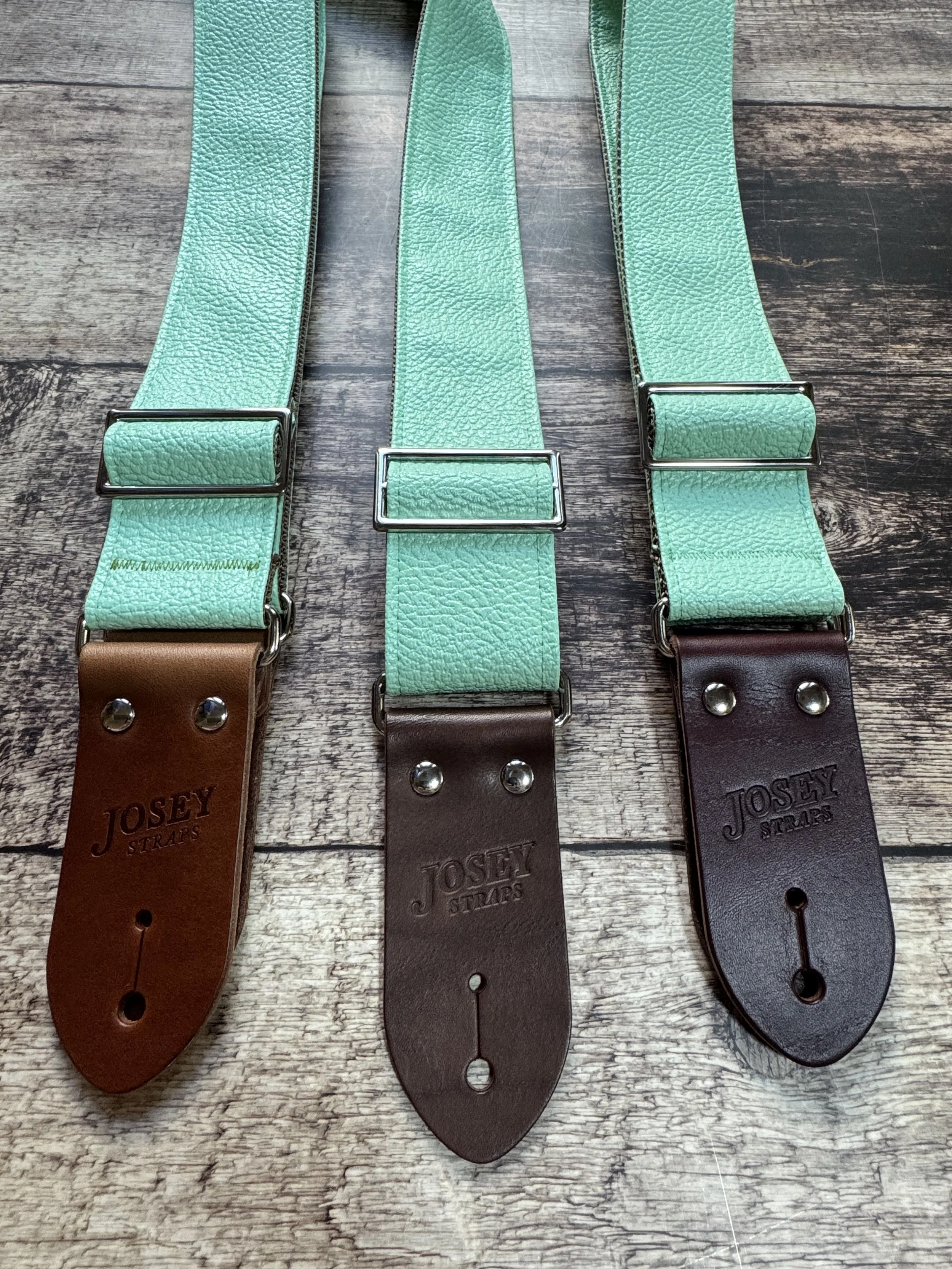 Seafoam green guitar straps on wooden floor.