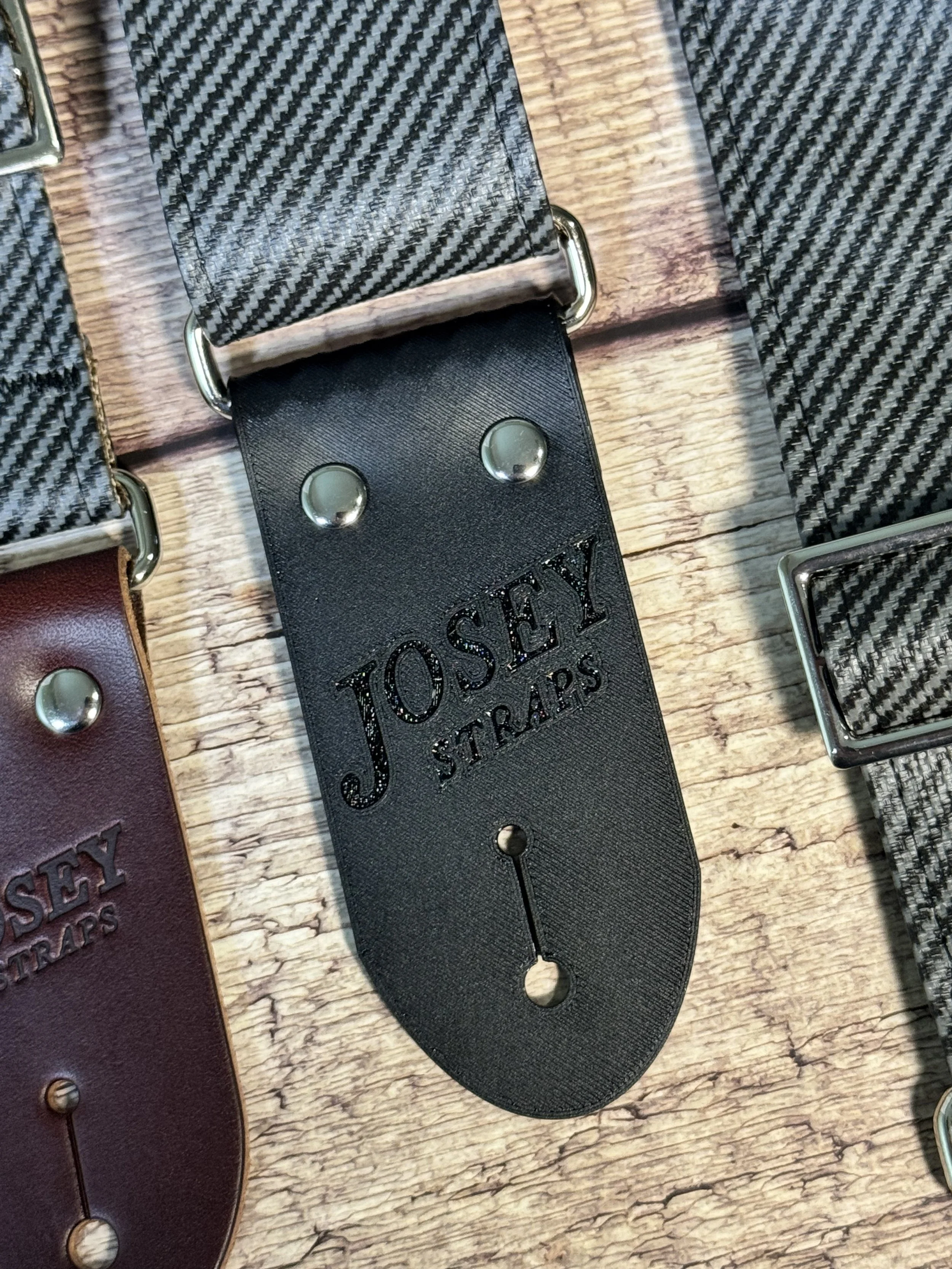 Close up shot of charcoal tweed guitar straps on wooden floor.