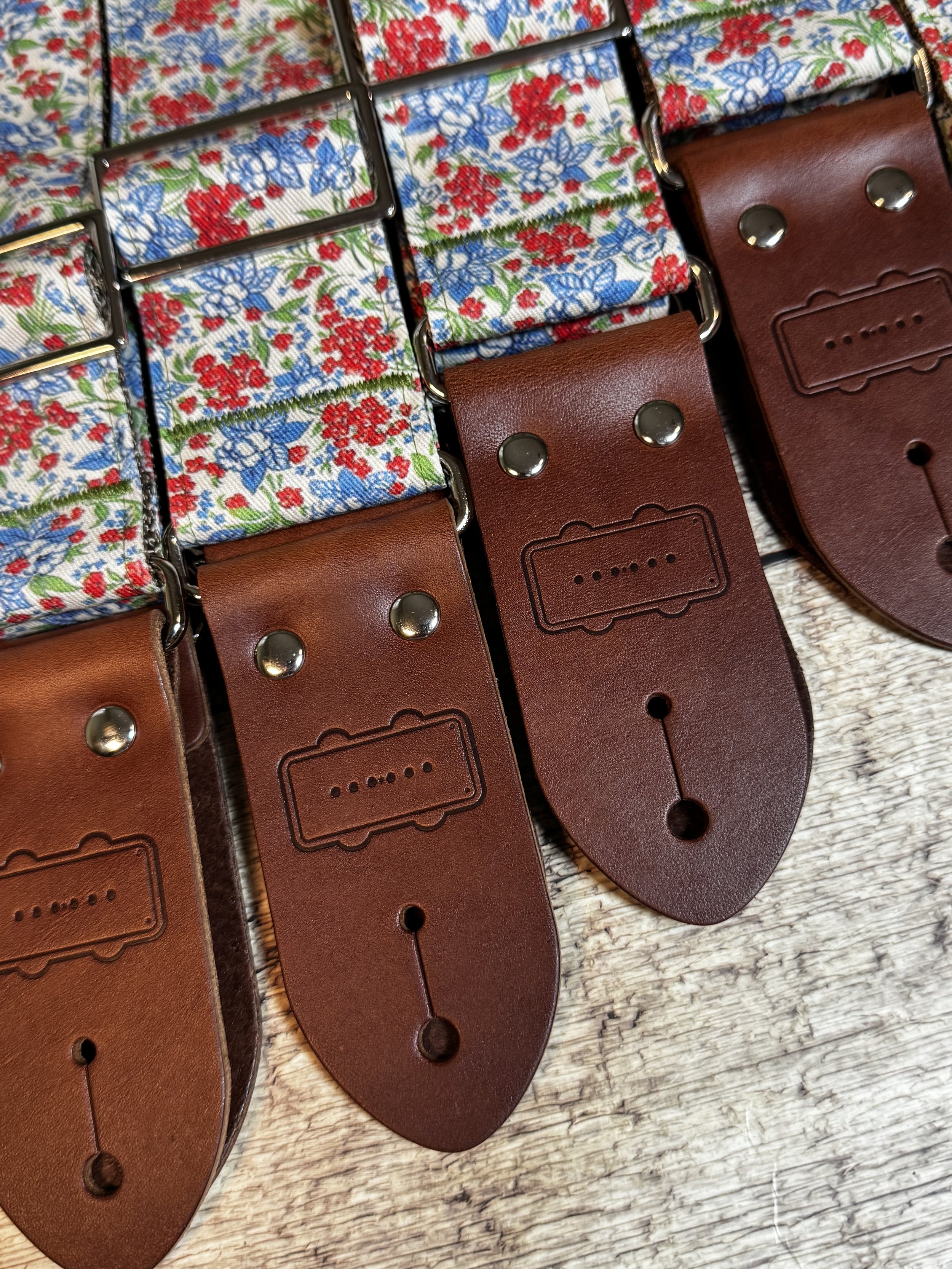 Close-up of guitar straps with leather ends embossed with Black Bobbin's logo stamped on the leather.