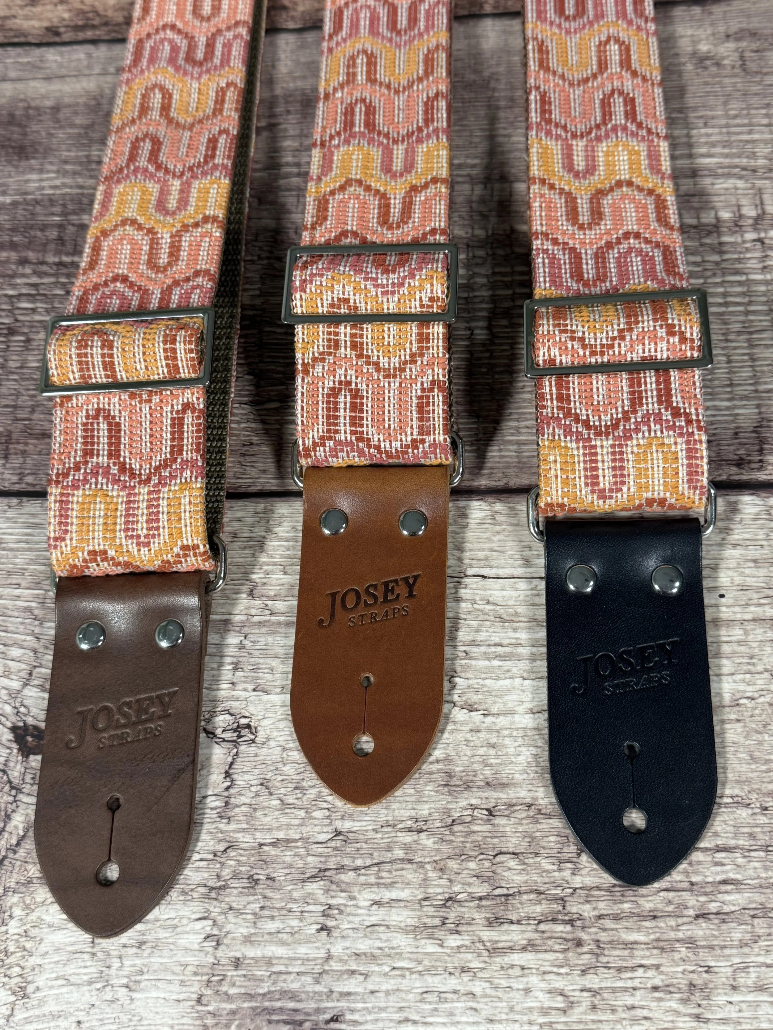 Vintage disco-inspired woven guitar straps in terracotta and gold tones by Josey Straps.  These straps are set on wood backdrop.