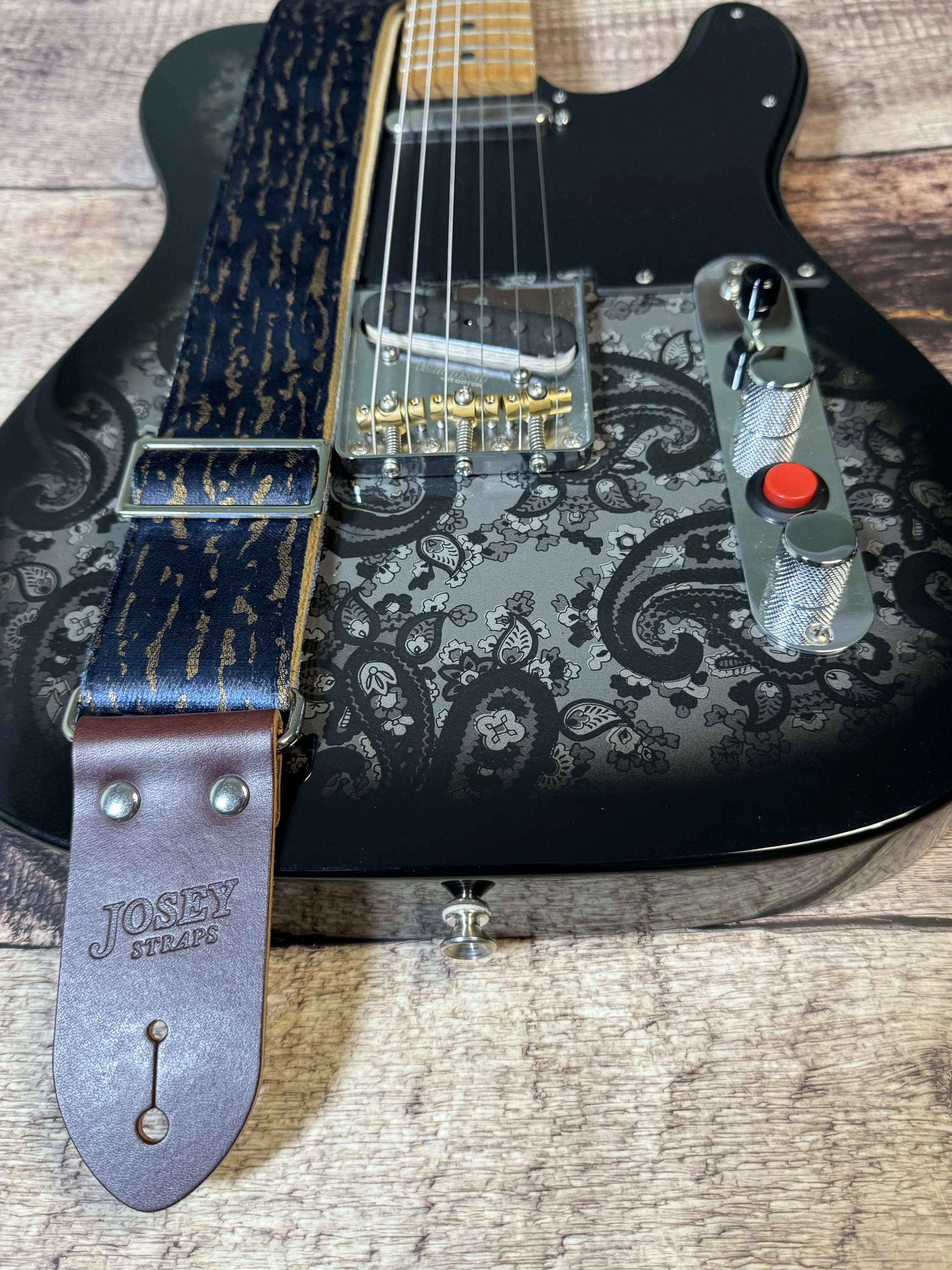 Blue and gold guitar strap laid over a black paisley telecaster guitar.