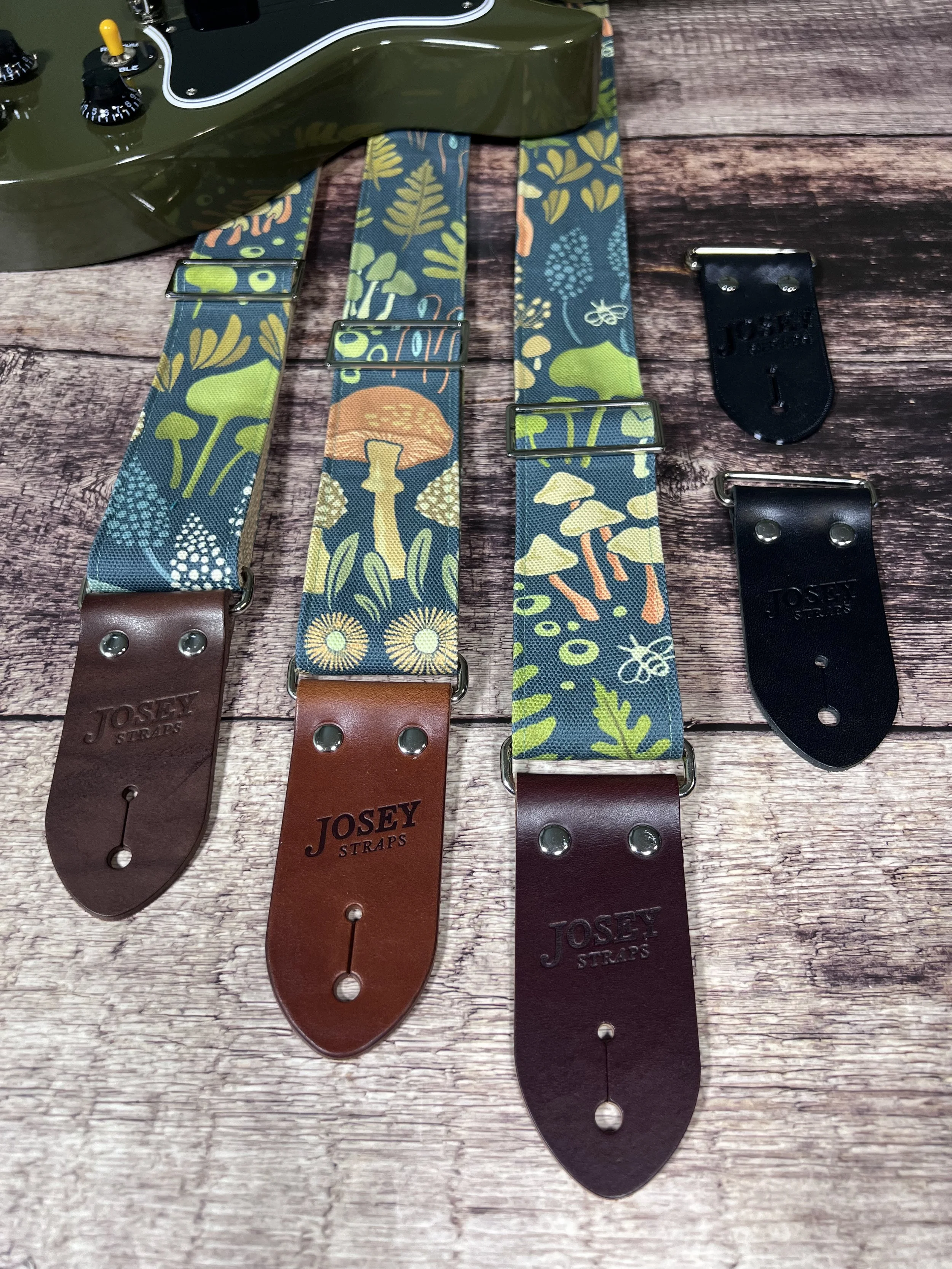 Dark botanical guitar straps on wooden backdrop.