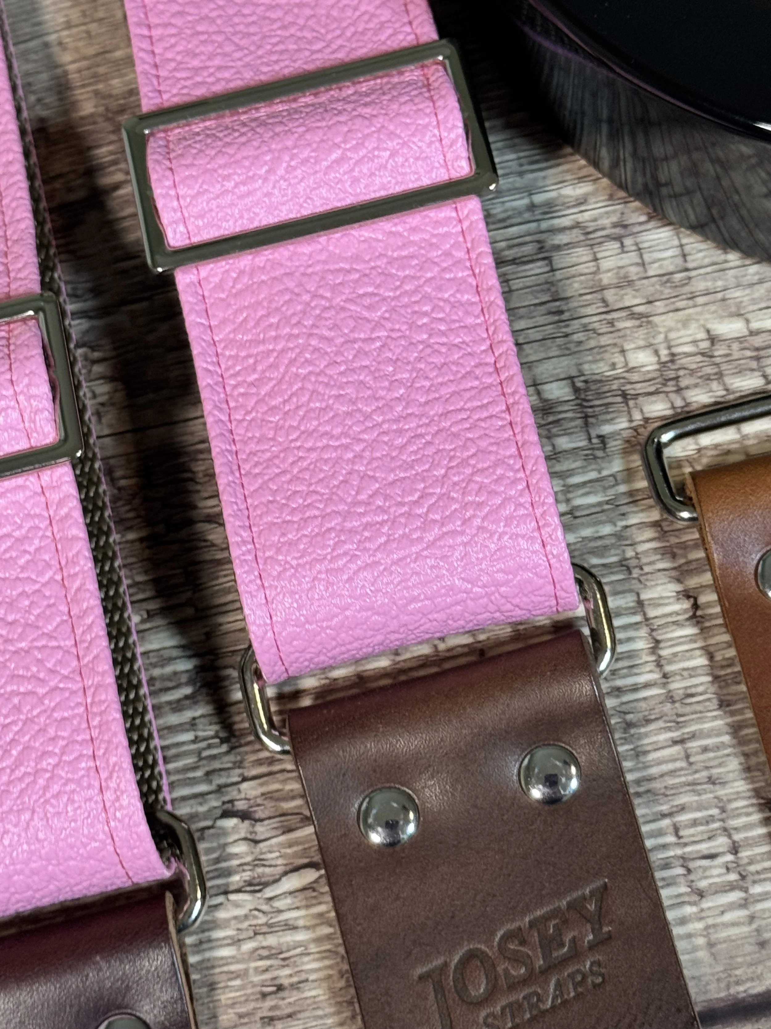 Up close shot of Bubblegum pink tolex guitar straps on wooden floor.