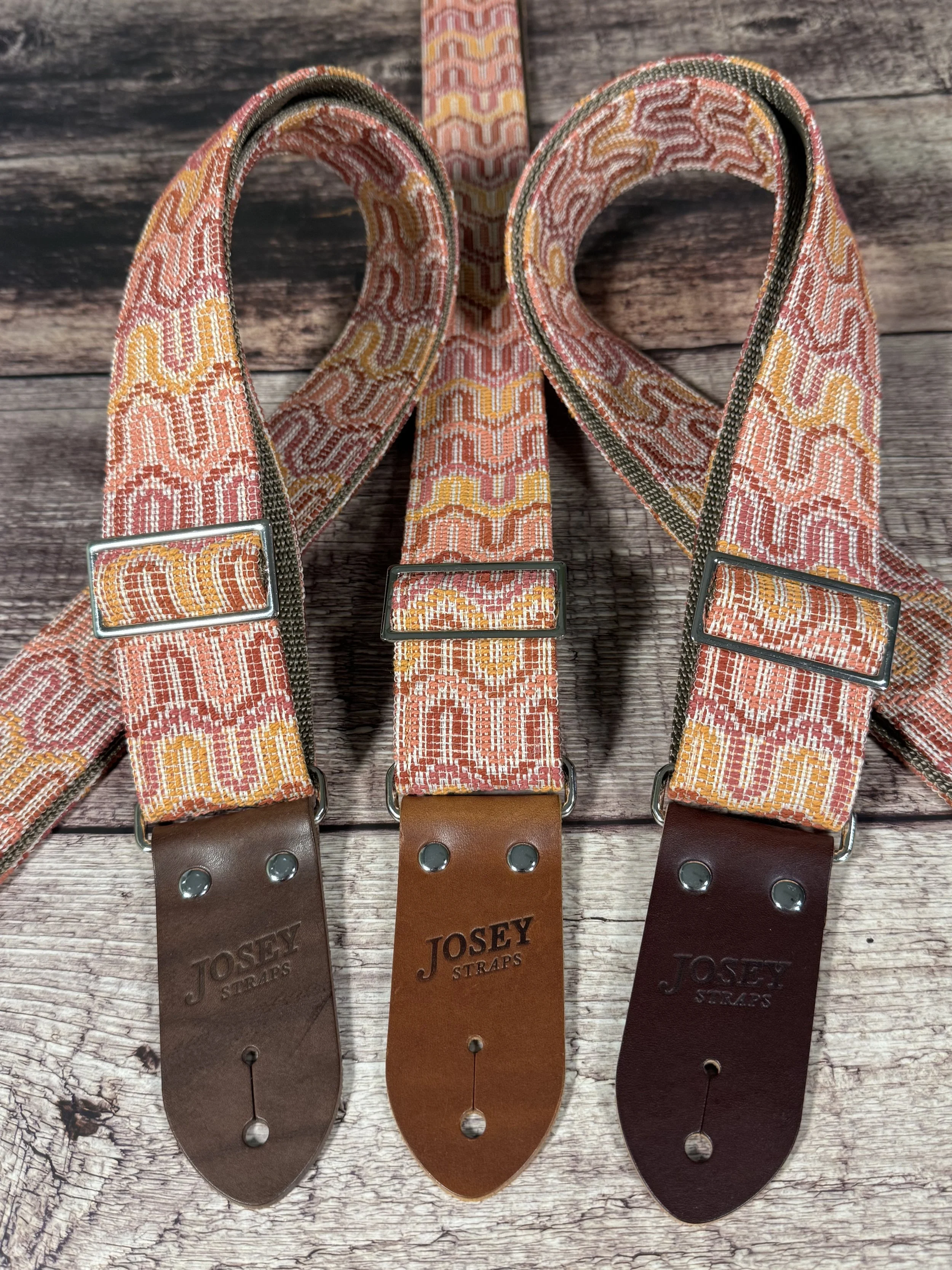 Vintage disco-inspired woven guitar straps in terracotta and gold tones by Josey Straps.  These straps are set on wood backdrop.