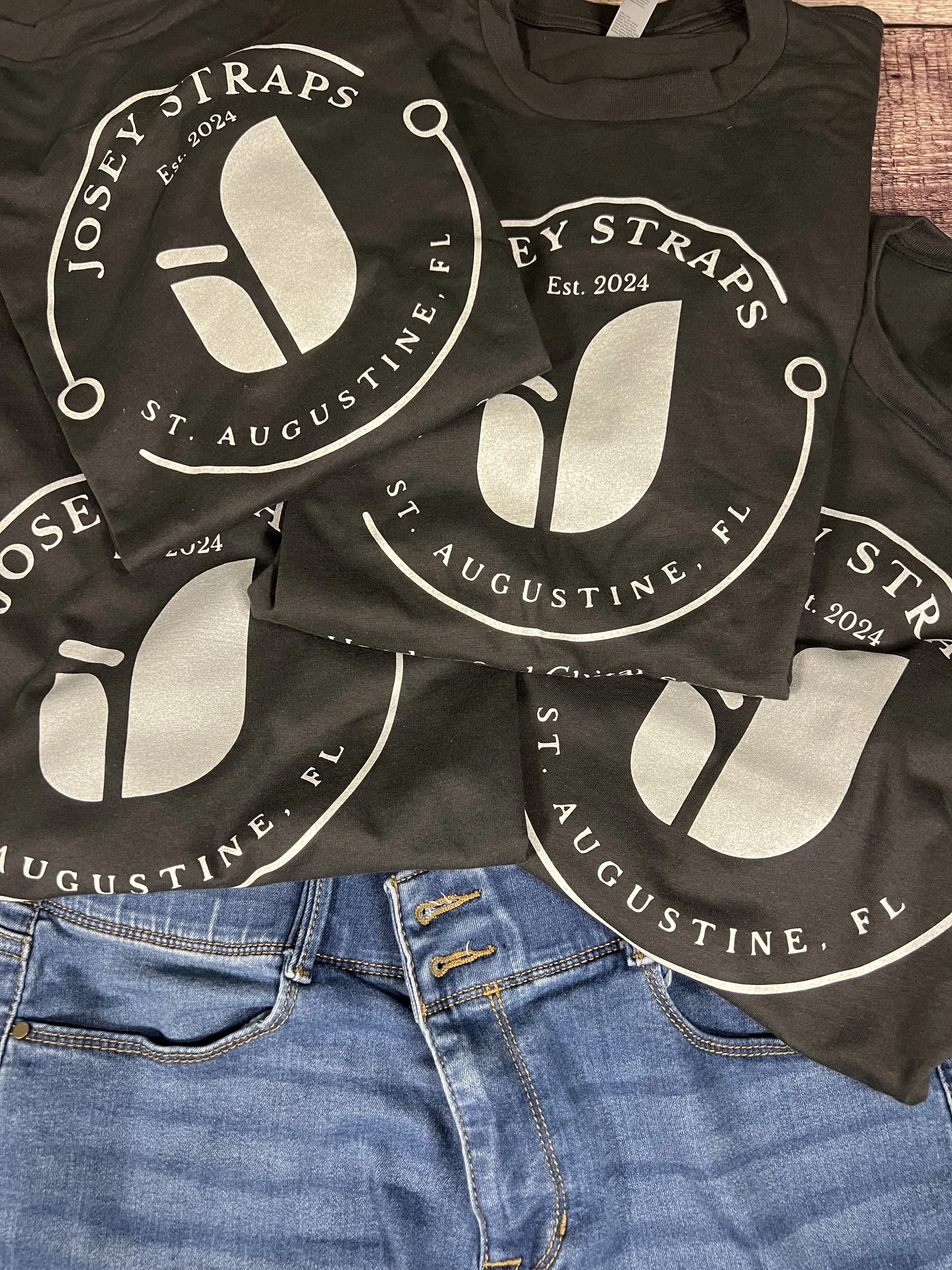 Vintage black Josey Straps screen printed t-shirts paired with denim jeans arranged on a wooden floor backdrop.