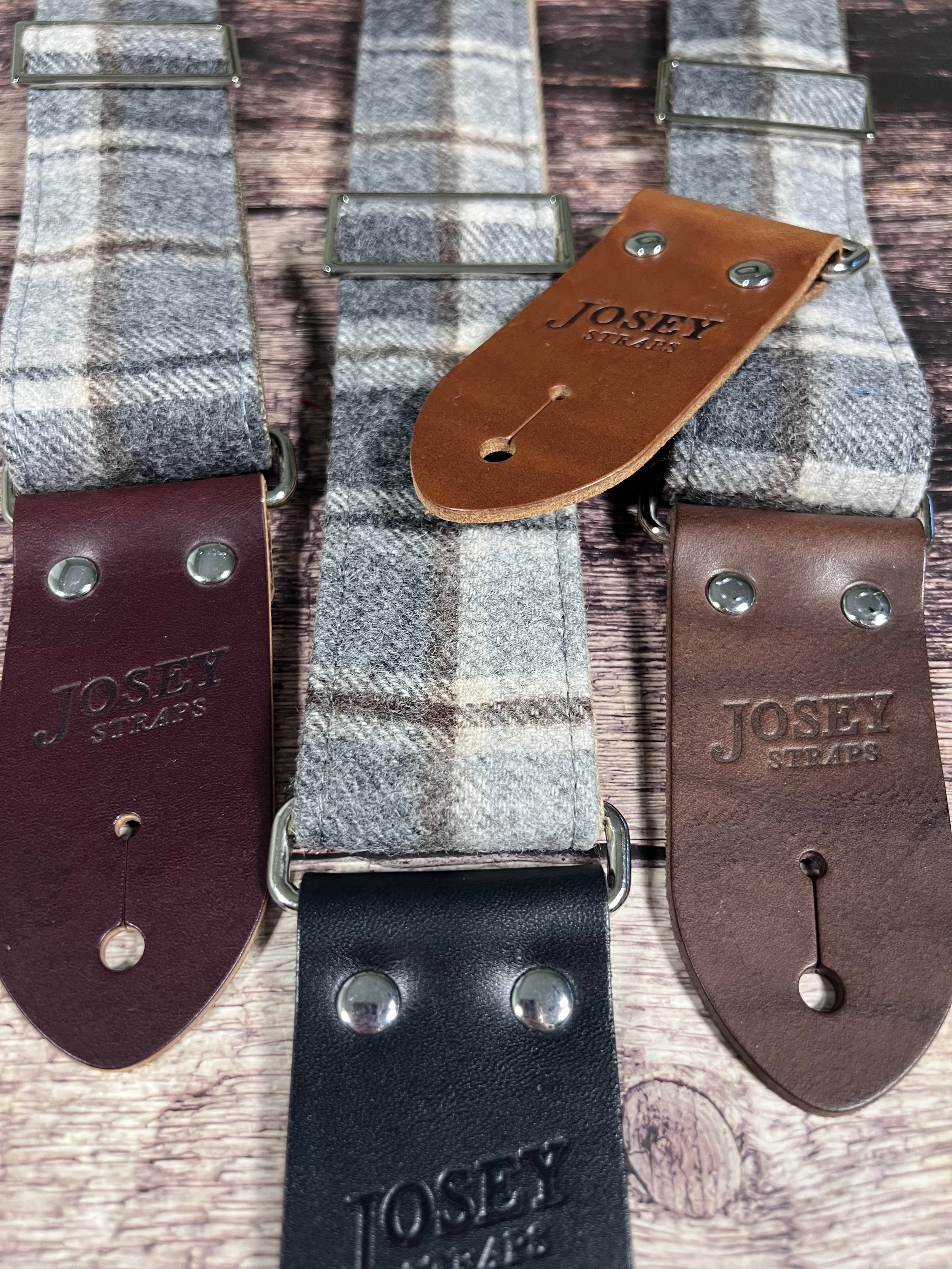 Vintage style grey plaid guitar straps on wooden floor.