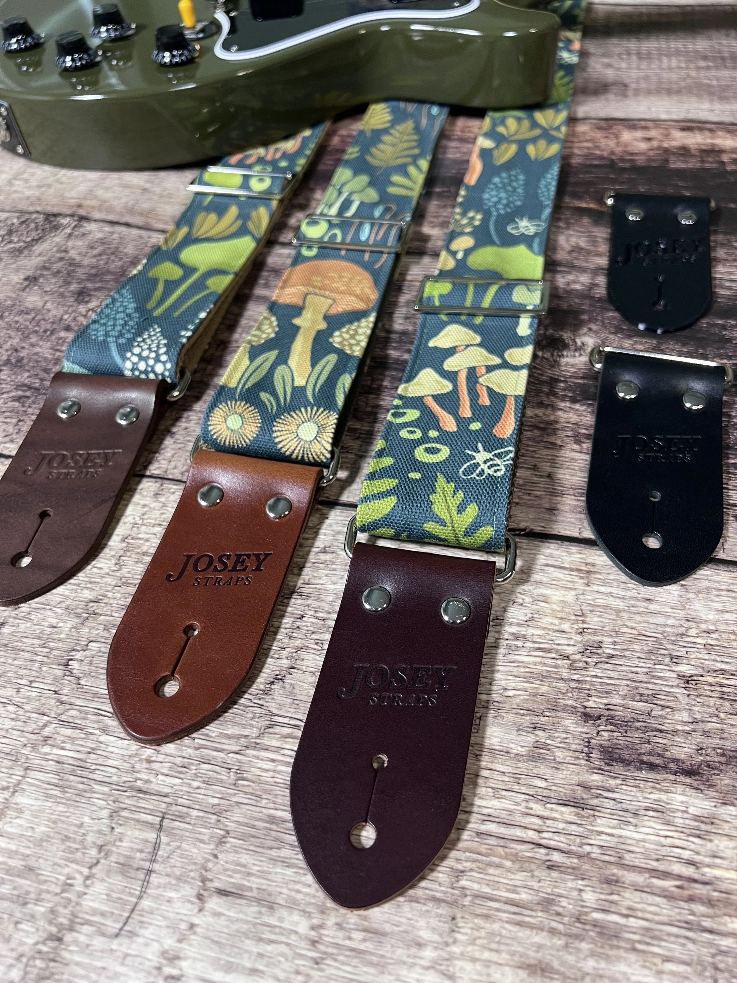 Dark botanical guitar straps on wooden backdrop.