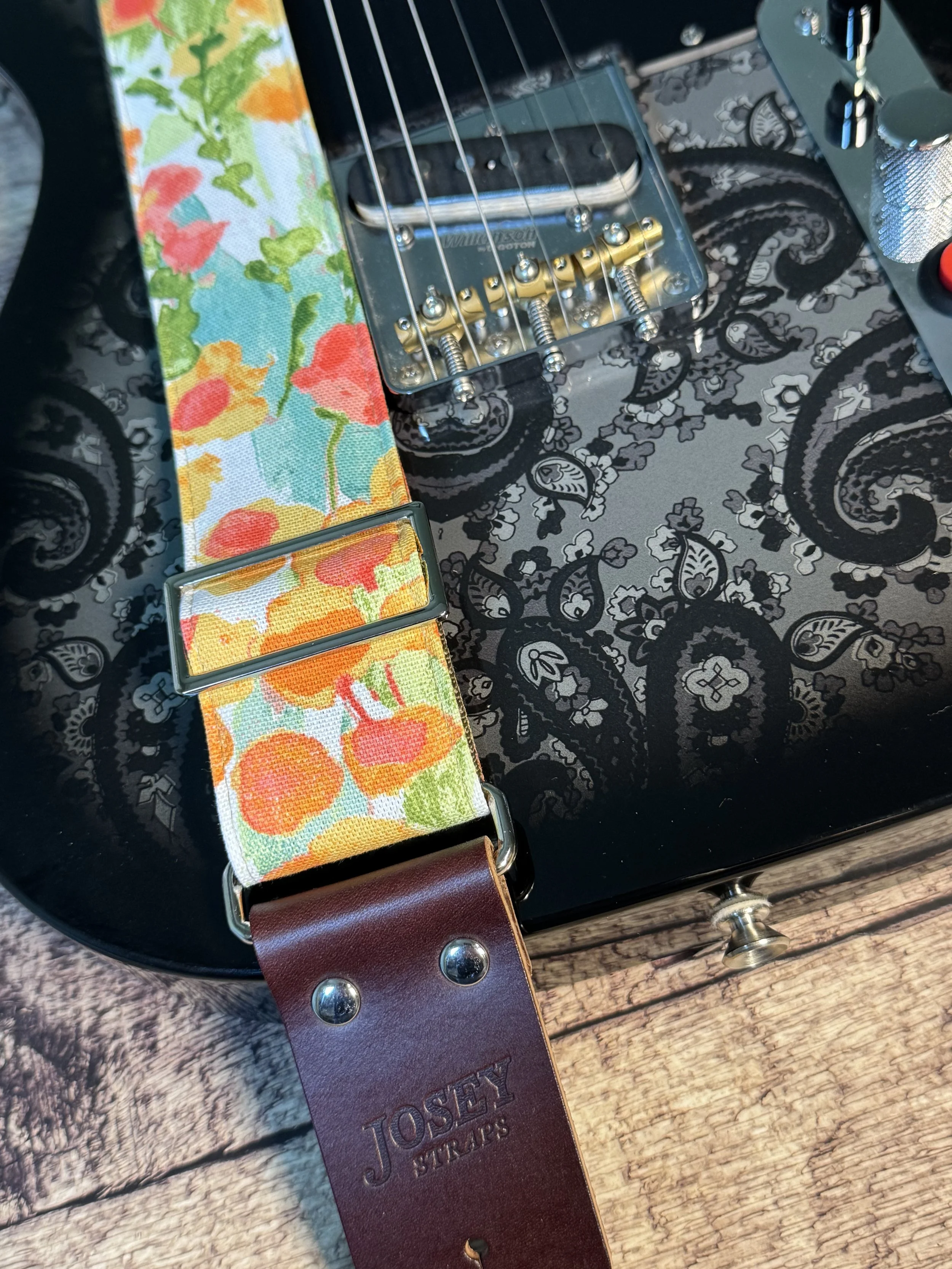 Floral guitar strap on black paisley telecaster guitar.