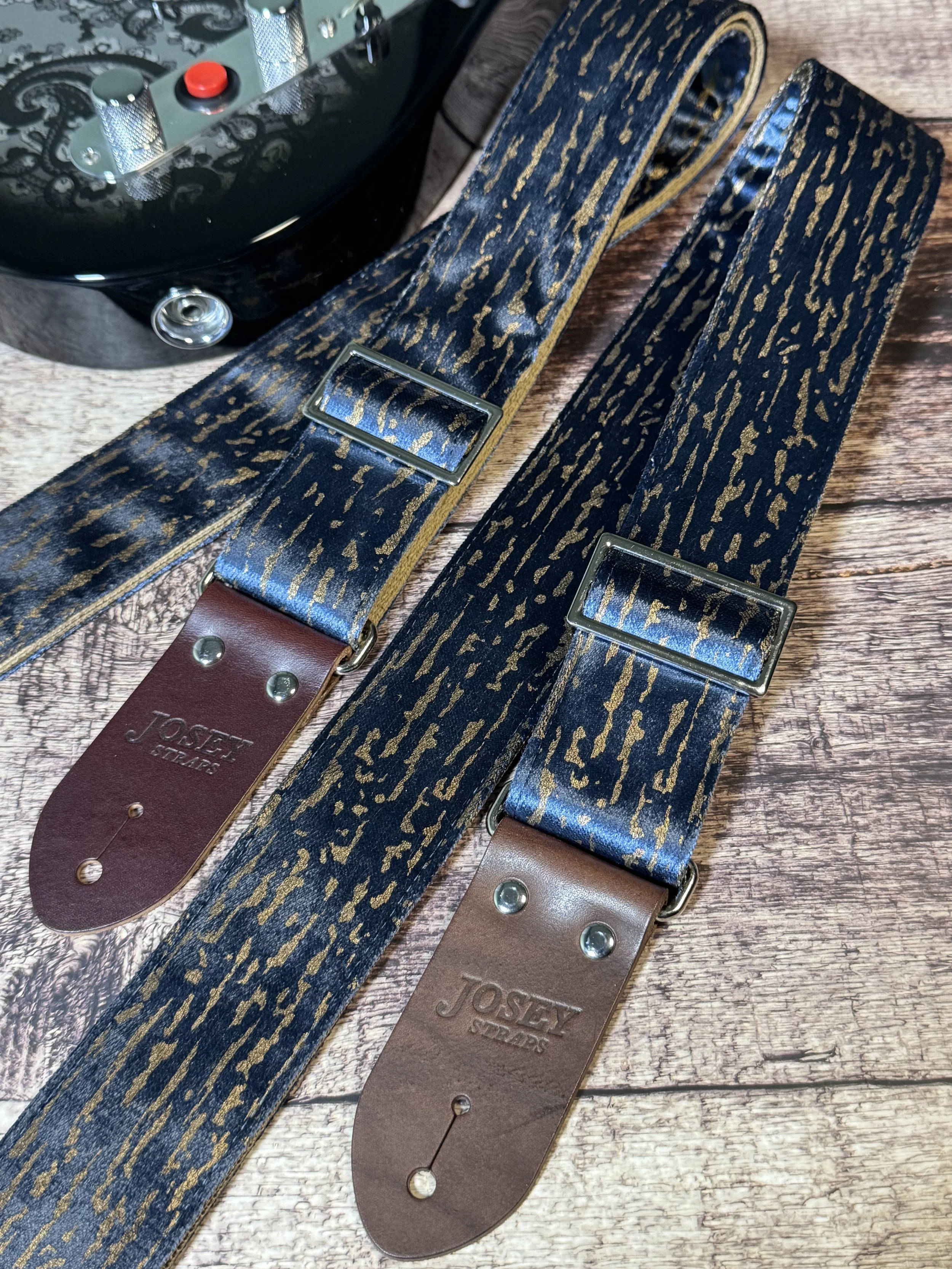 Blue and gold guitar straps on a wooden floor backdrop.