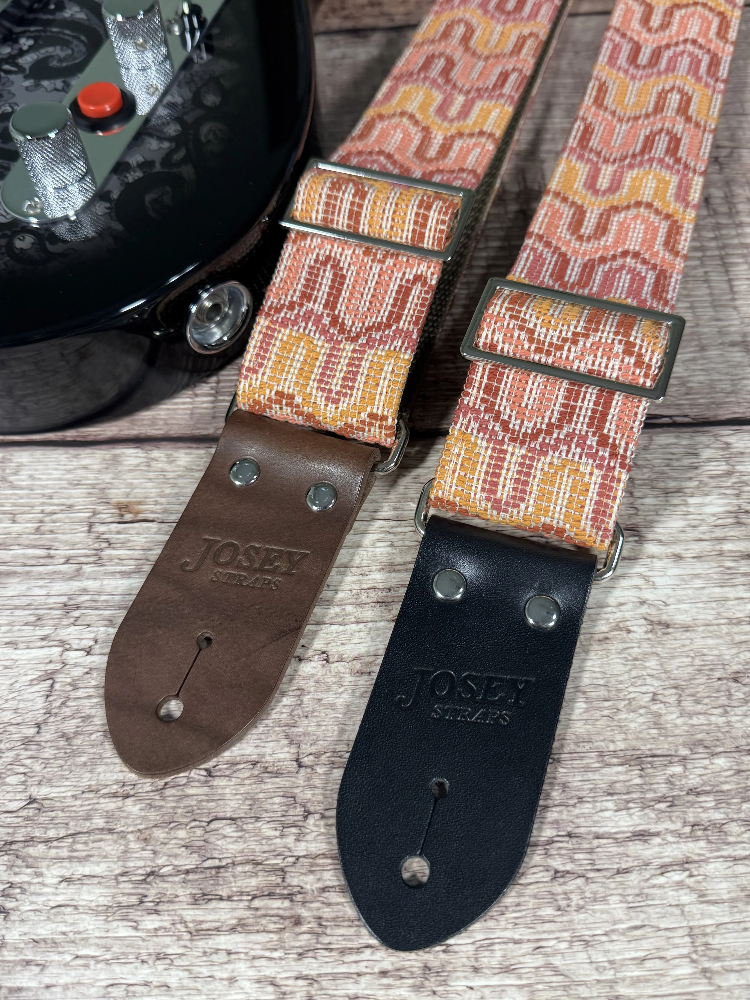 Vintage disco-inspired woven guitar straps in terracotta and gold tones by Josey Straps.  These straps are set on wood backdrop.