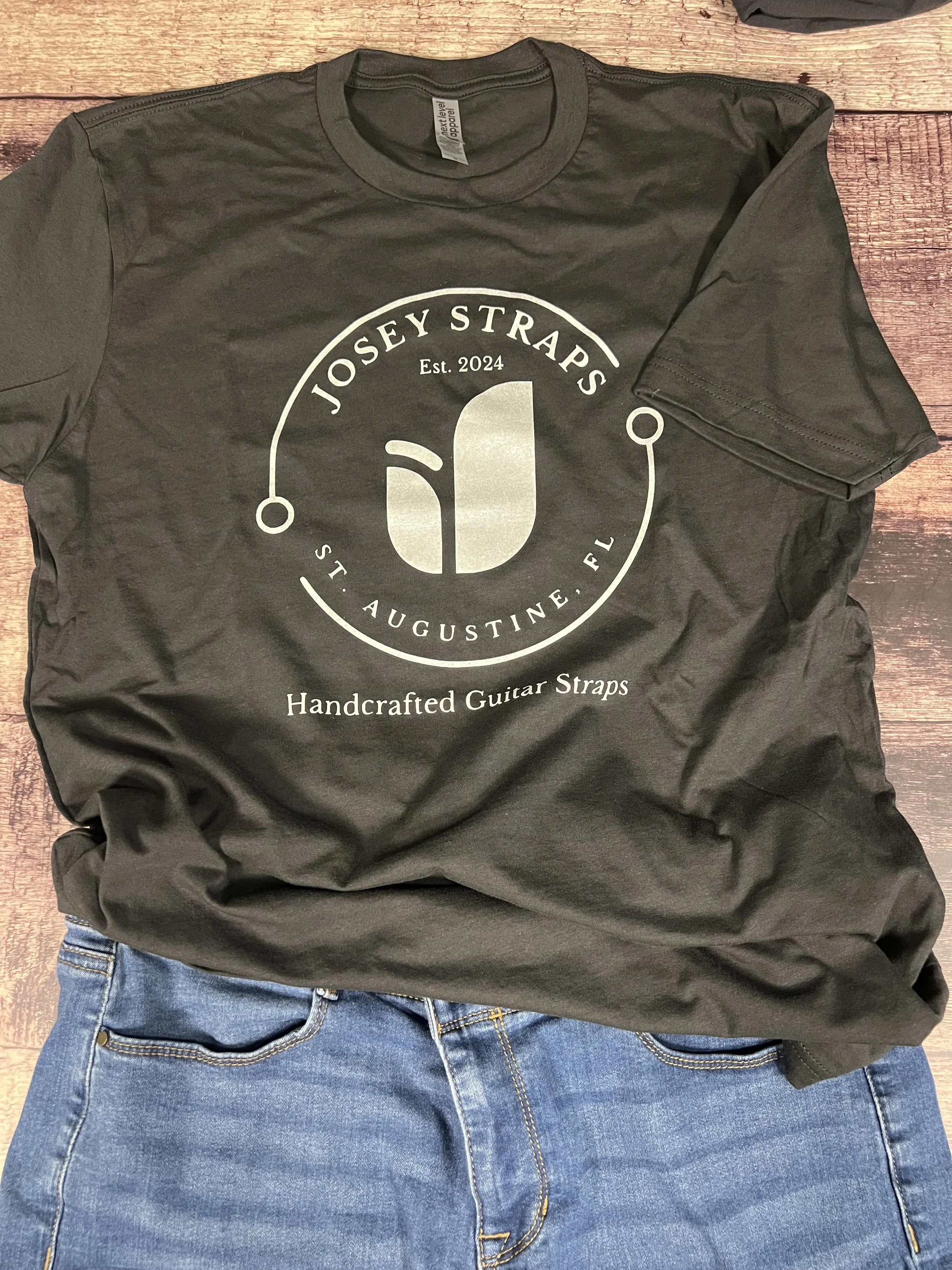 Vintage black Josey Straps screen printed t-shirt paired with denim jeans arranged on a wooden floor backdrop.