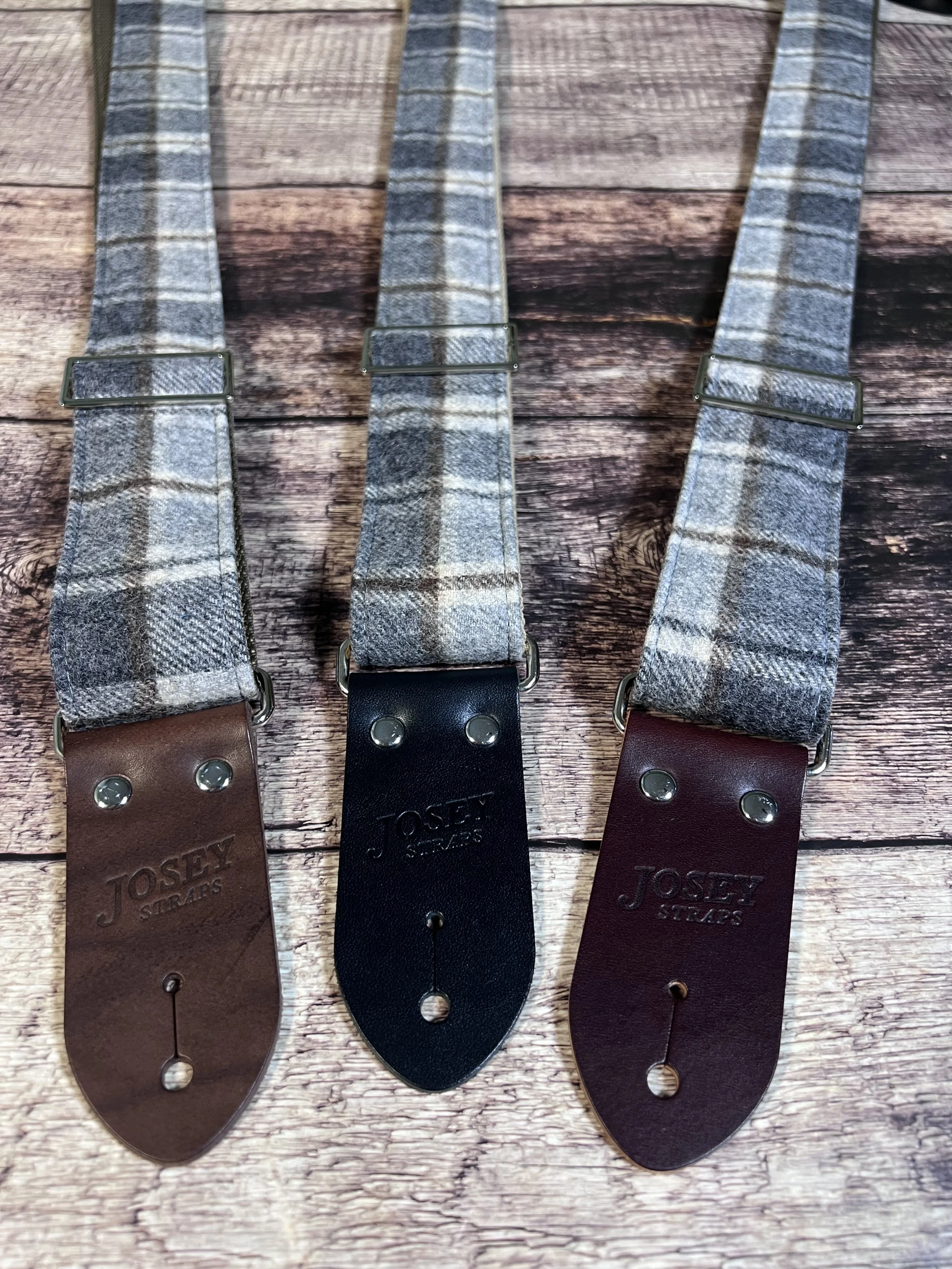 Vintage style grey plaid guitar straps on wooden floor.
