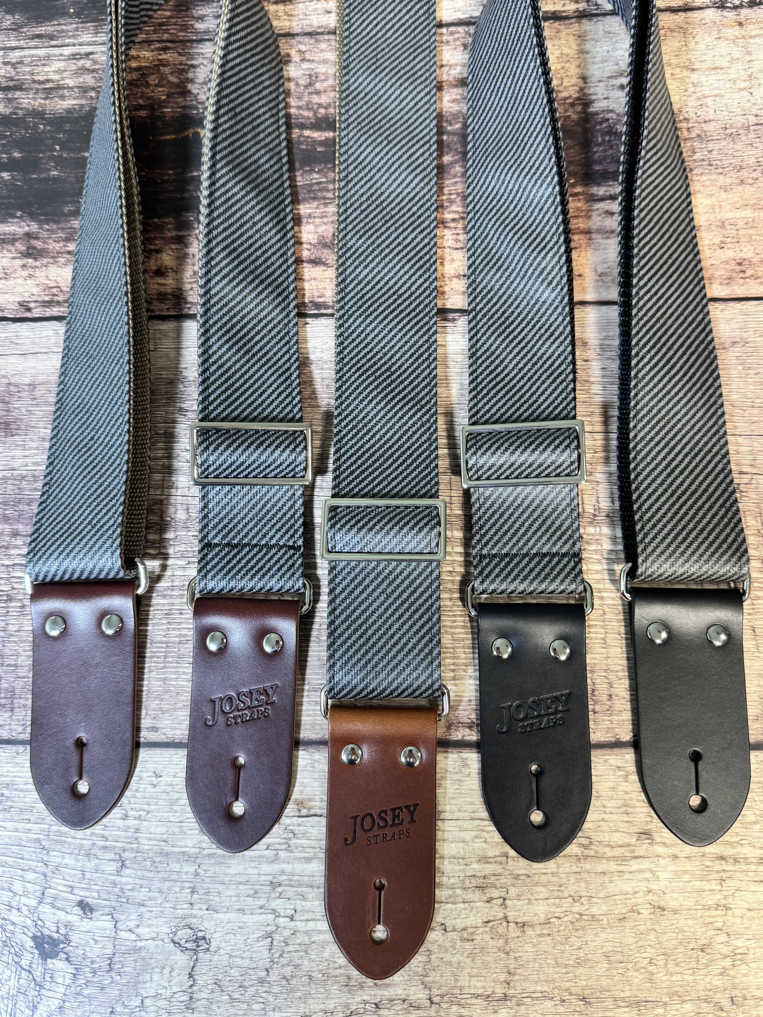 Charcoal tweed guitar straps on wooden floor.