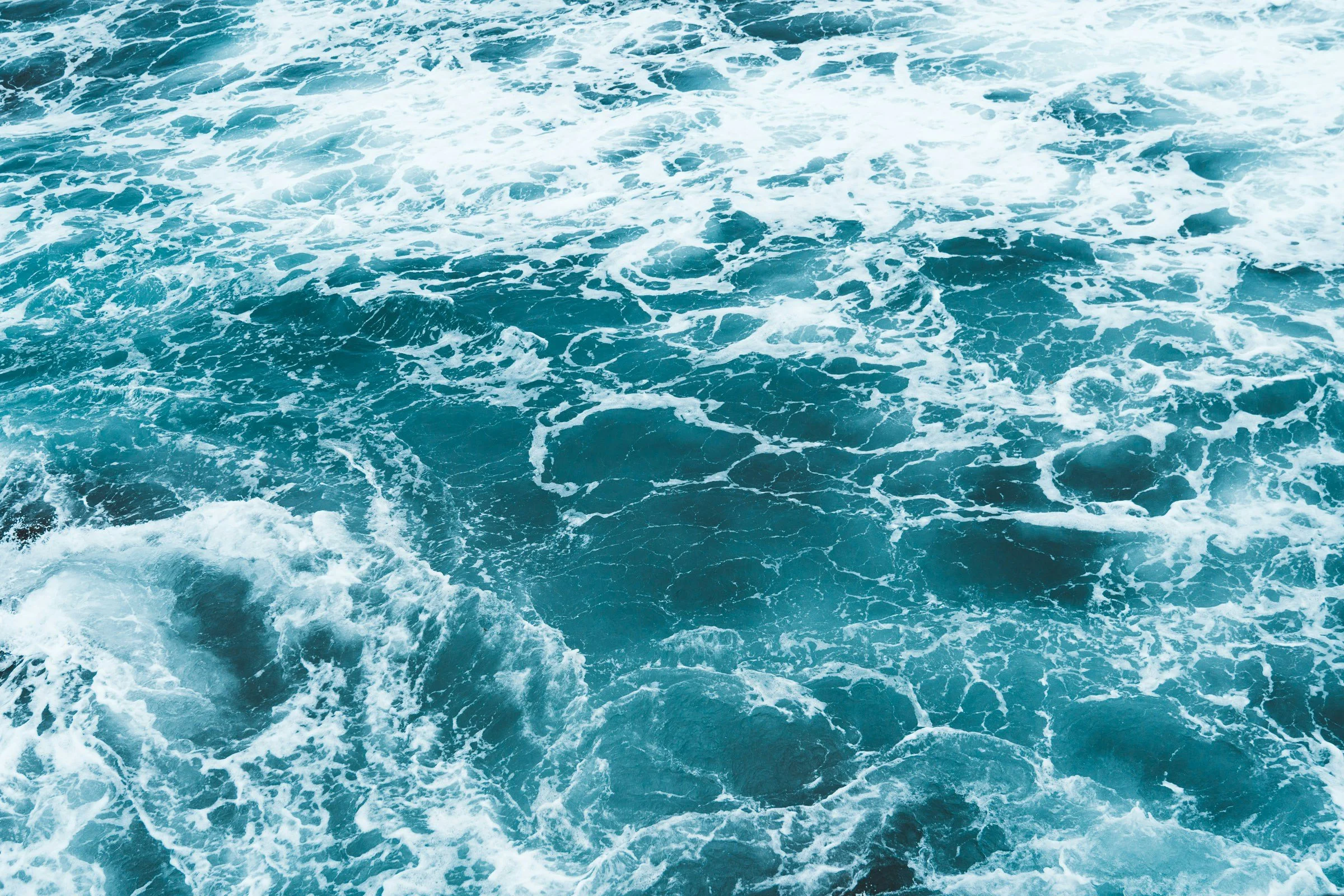 Aerial view of blue ocean water with white foam and waves.