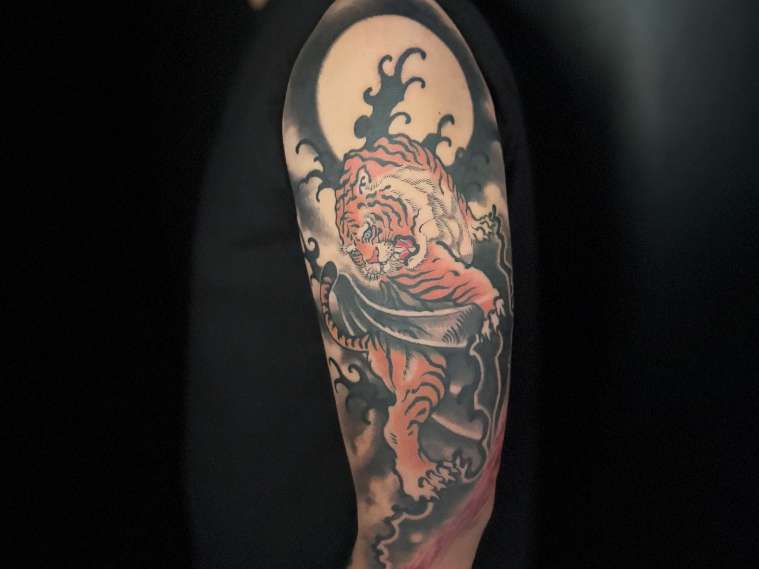 Close-up of a colorful traditional Japanese-style tiger tattoo with waves and clouds on a person's upper arm