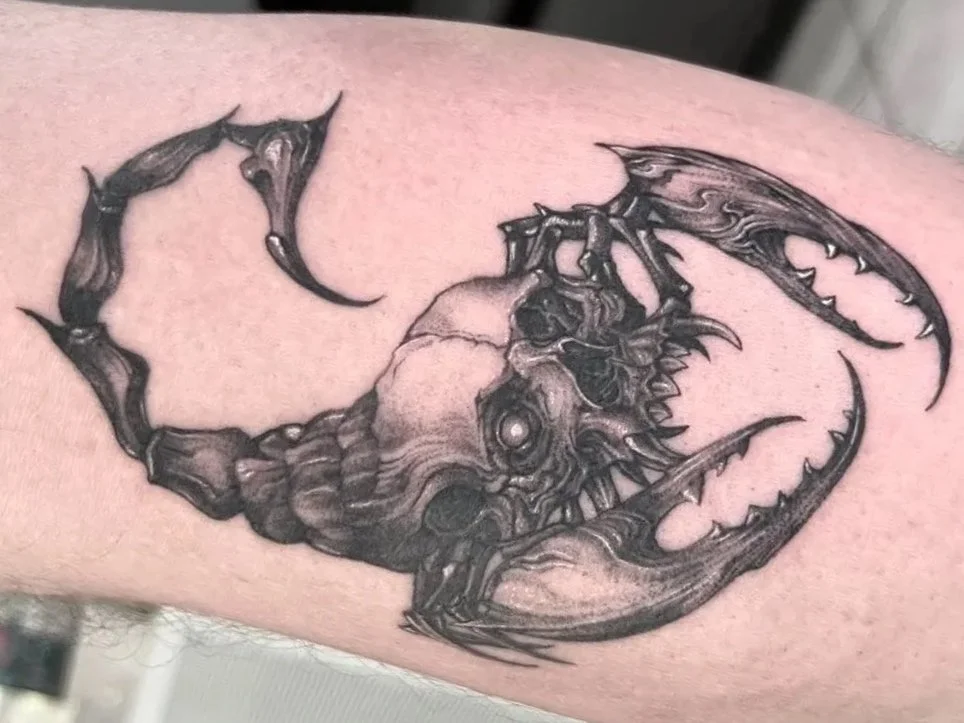 Detailed black-and-gray tattoo of a monstrous scorpion-like creature with curved pincers, wings, spikes, and a central eye.