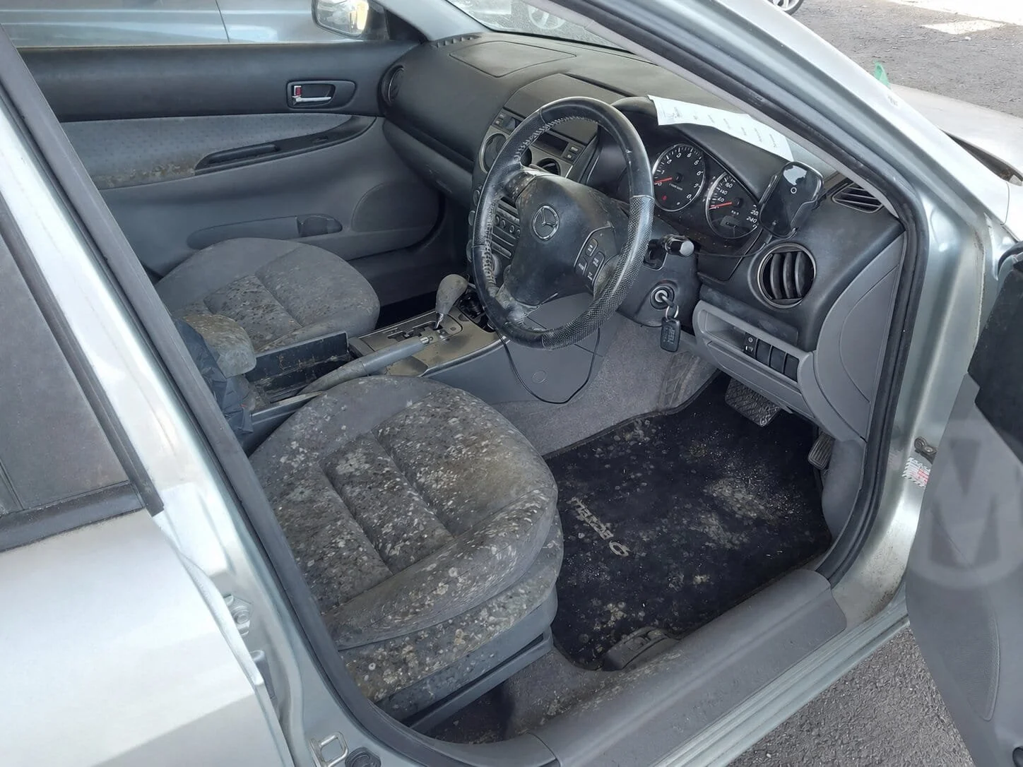 Mould-contaminated car interior before professional cleaning, showing heavy mould growth on the front seats, steering wheel, floor mat and dashboard area.