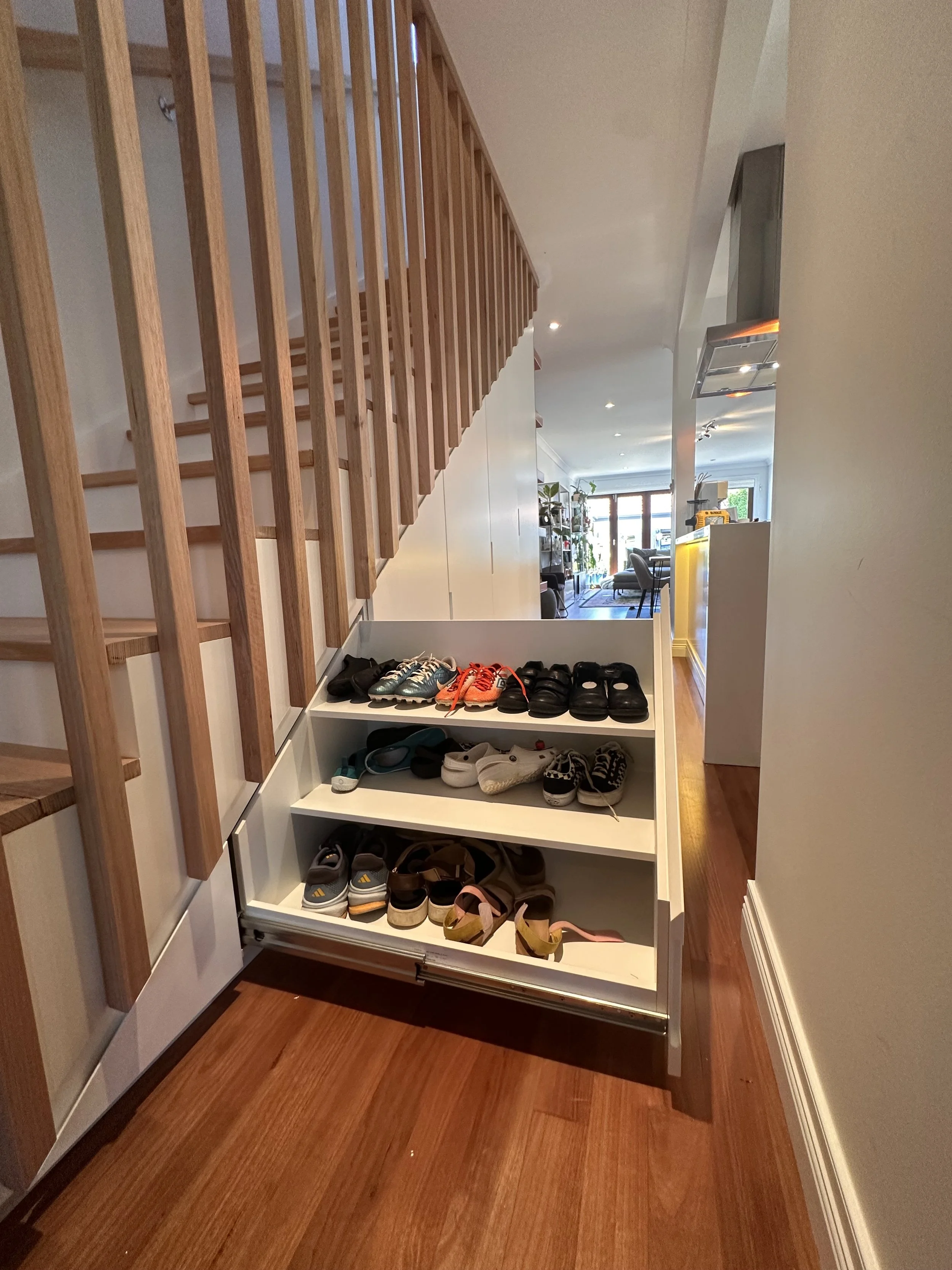 Custom shoe storage with open shelving under stairs cabinetry in satin finish