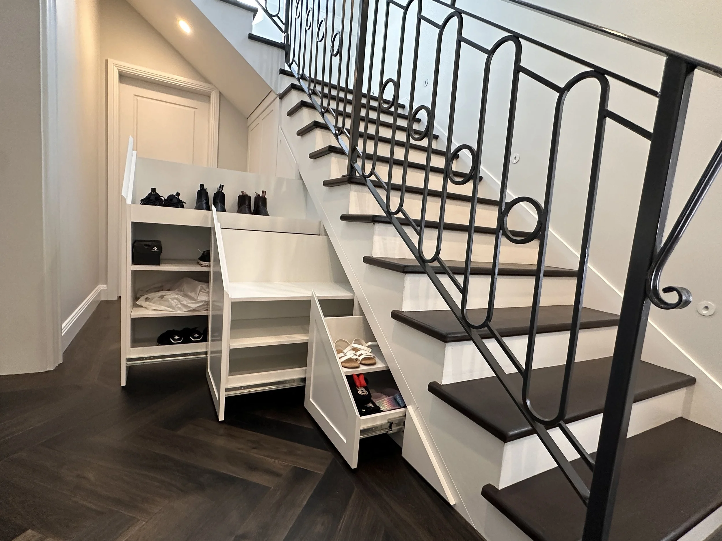 Custom under stairs cabinetry in white polyurethane with pull-out drawers for storage.