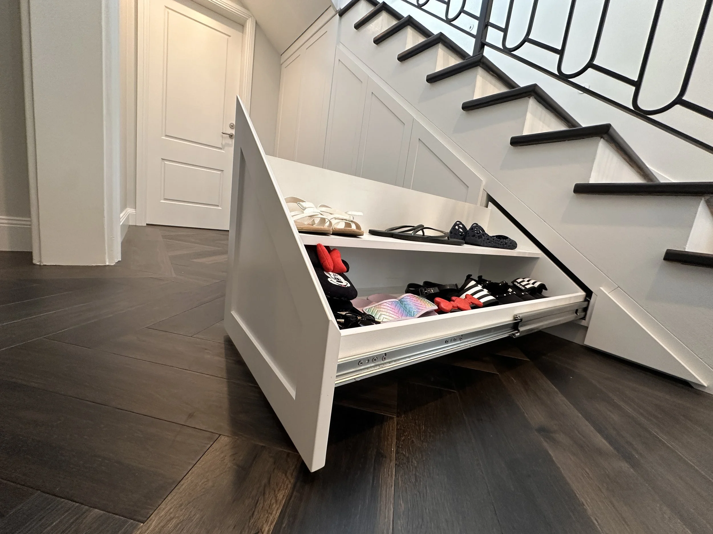 Custom white polyurethane under stairs cabinetry with pull-out drawers and open shelving for shoe storage