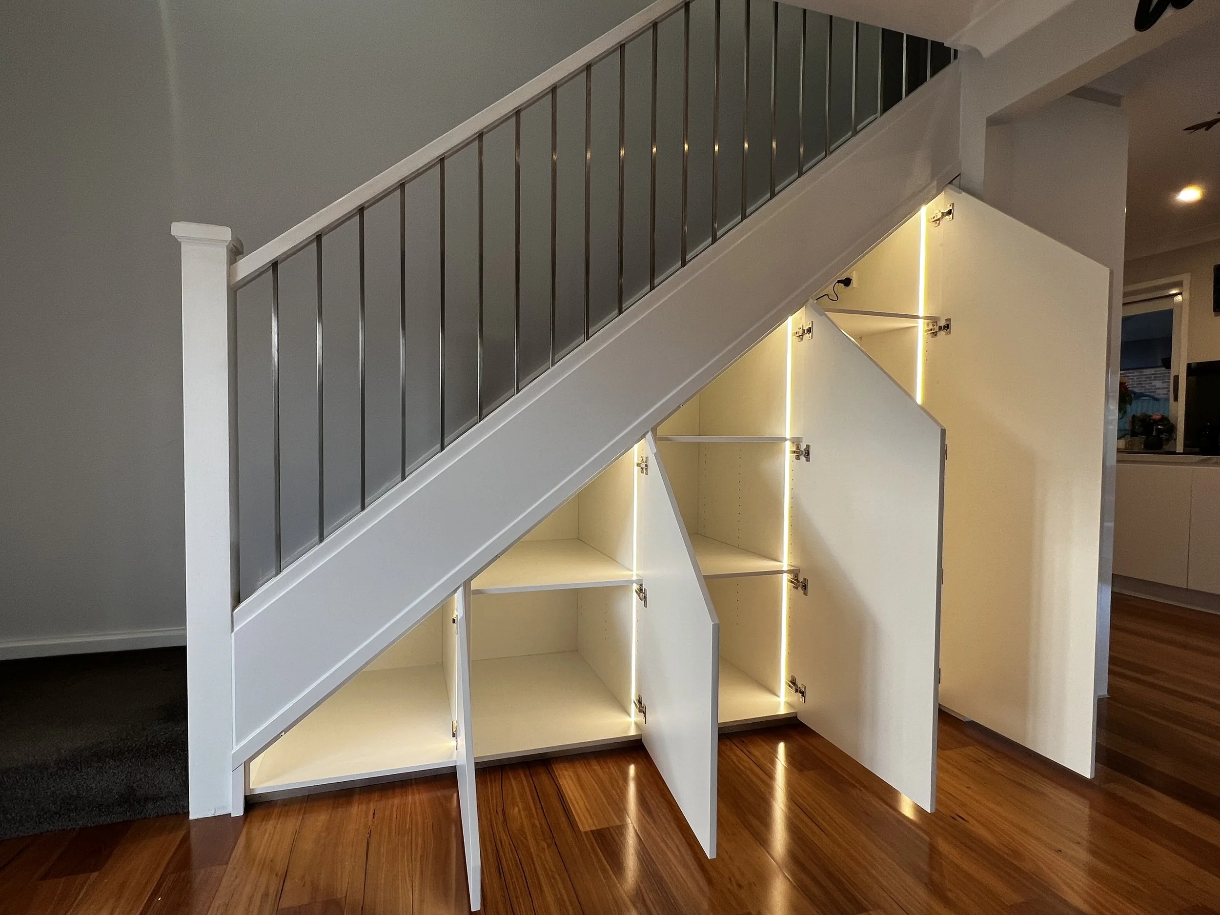 White polyurethane cabinetry under stairs with LED strip lighting inside