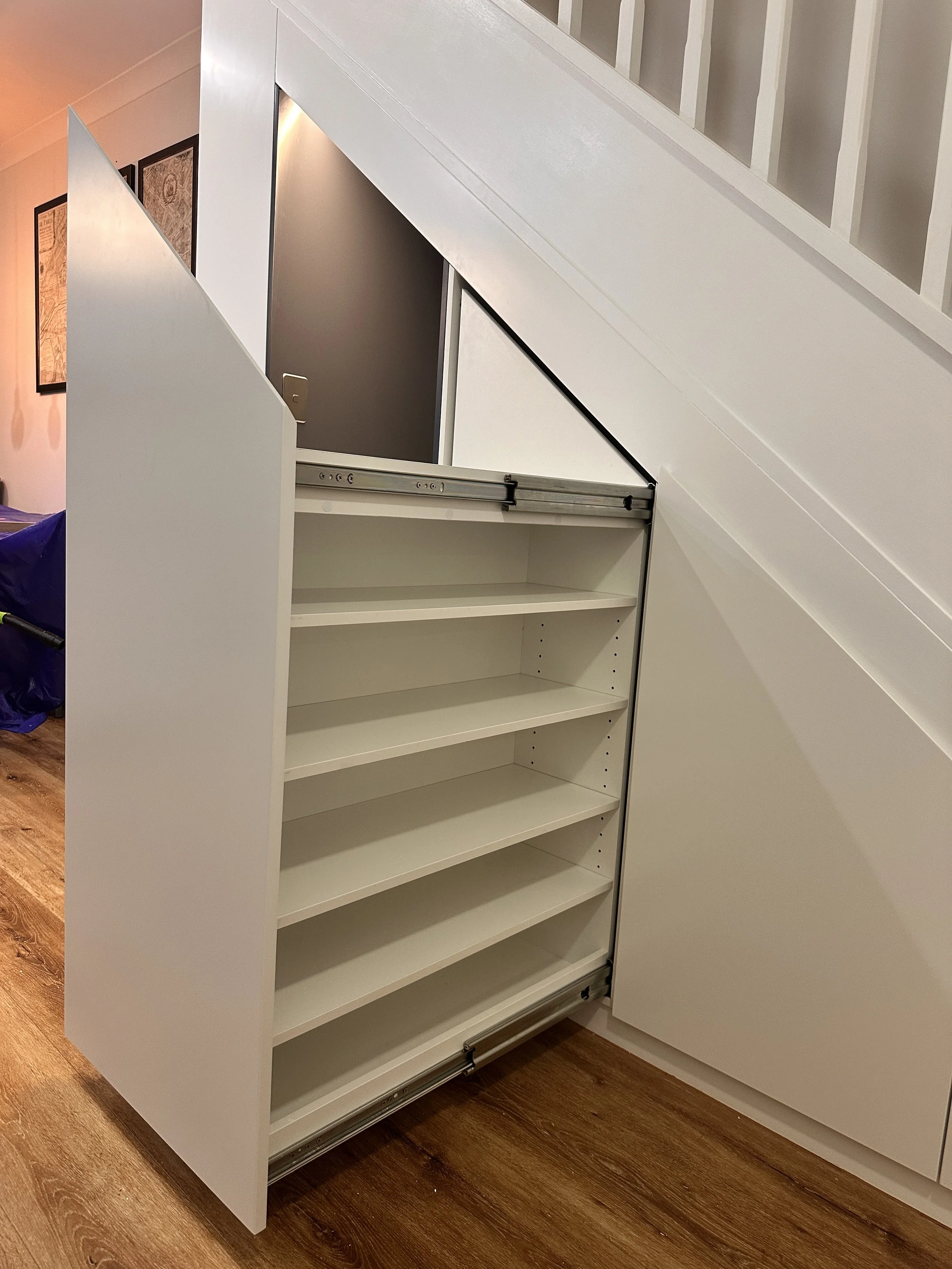 Custom under stairs cabinetry with open shelving and concealed drawers