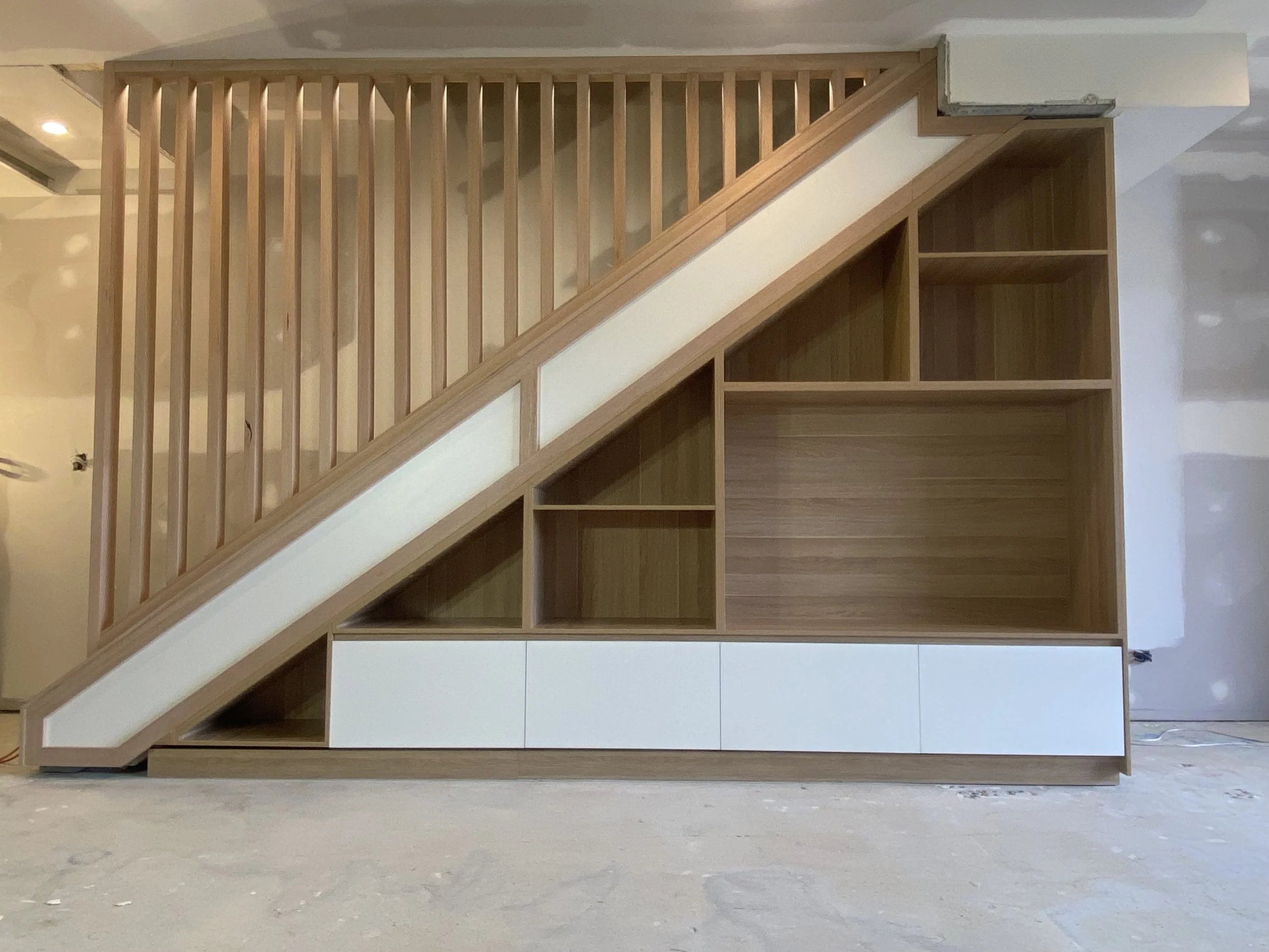 Under stairs cabinetry during installation with timber shelving and vertical slat balustrade design