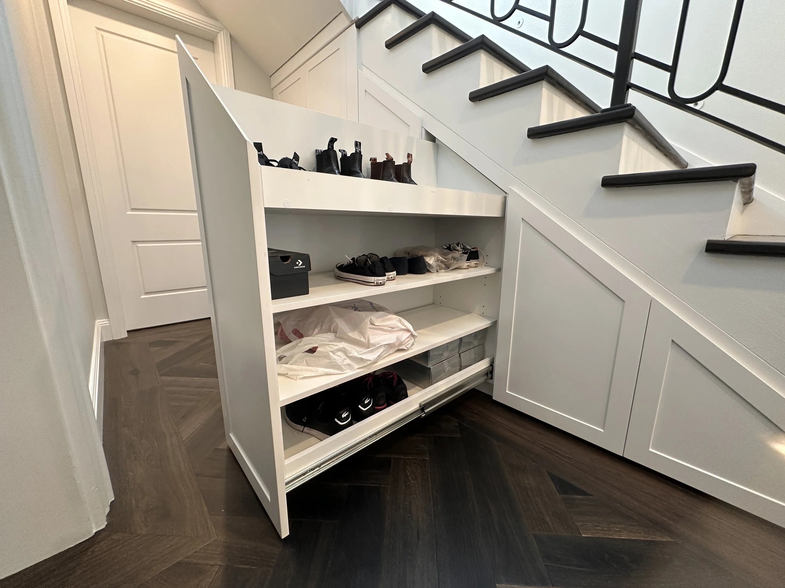 Custom white polyurethane under stairs cabinetry with pull-out drawers and open shelving for shoe storage