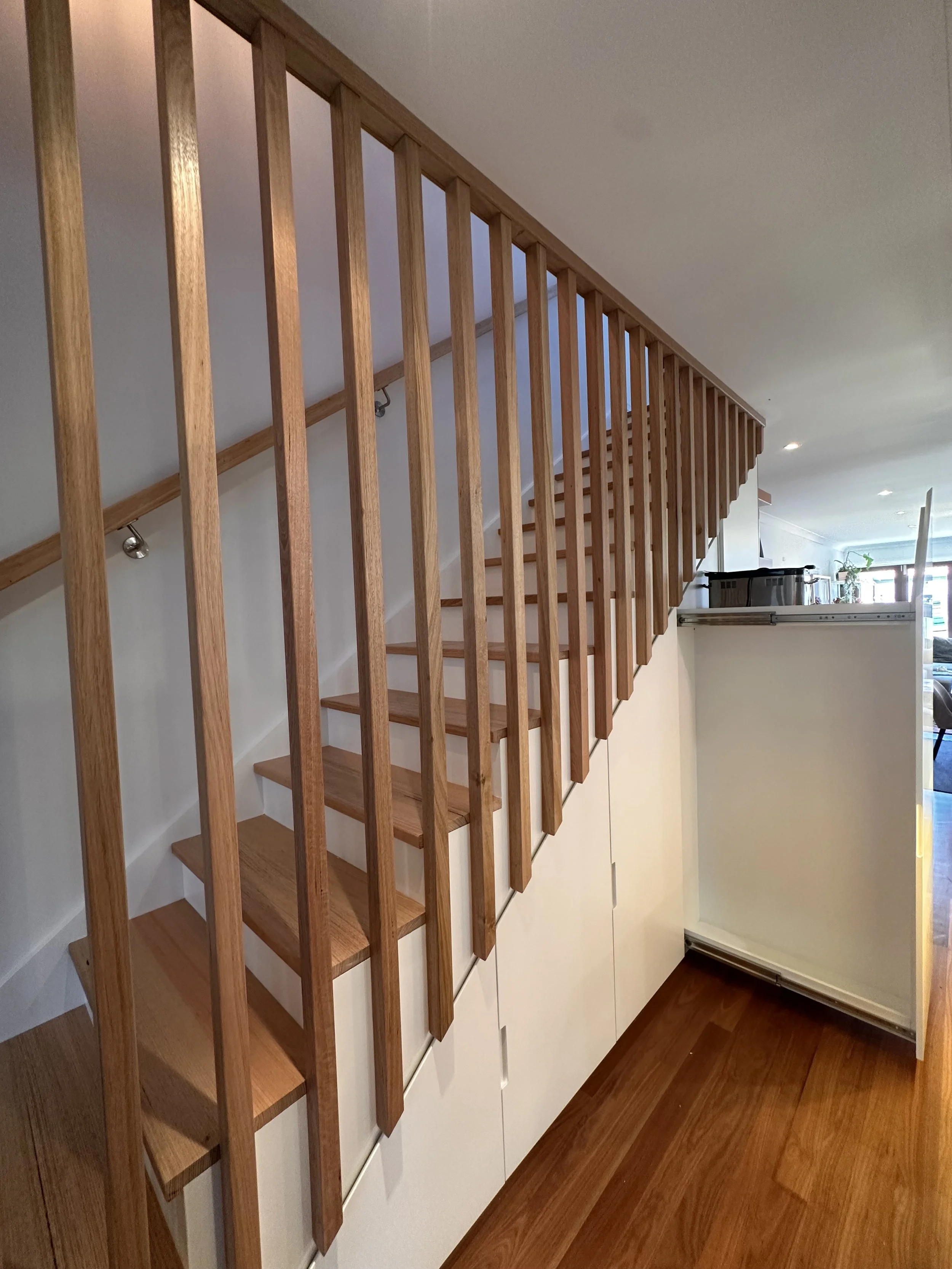 Custom under stairs cabinetry with hinged doors open to reveal shelving