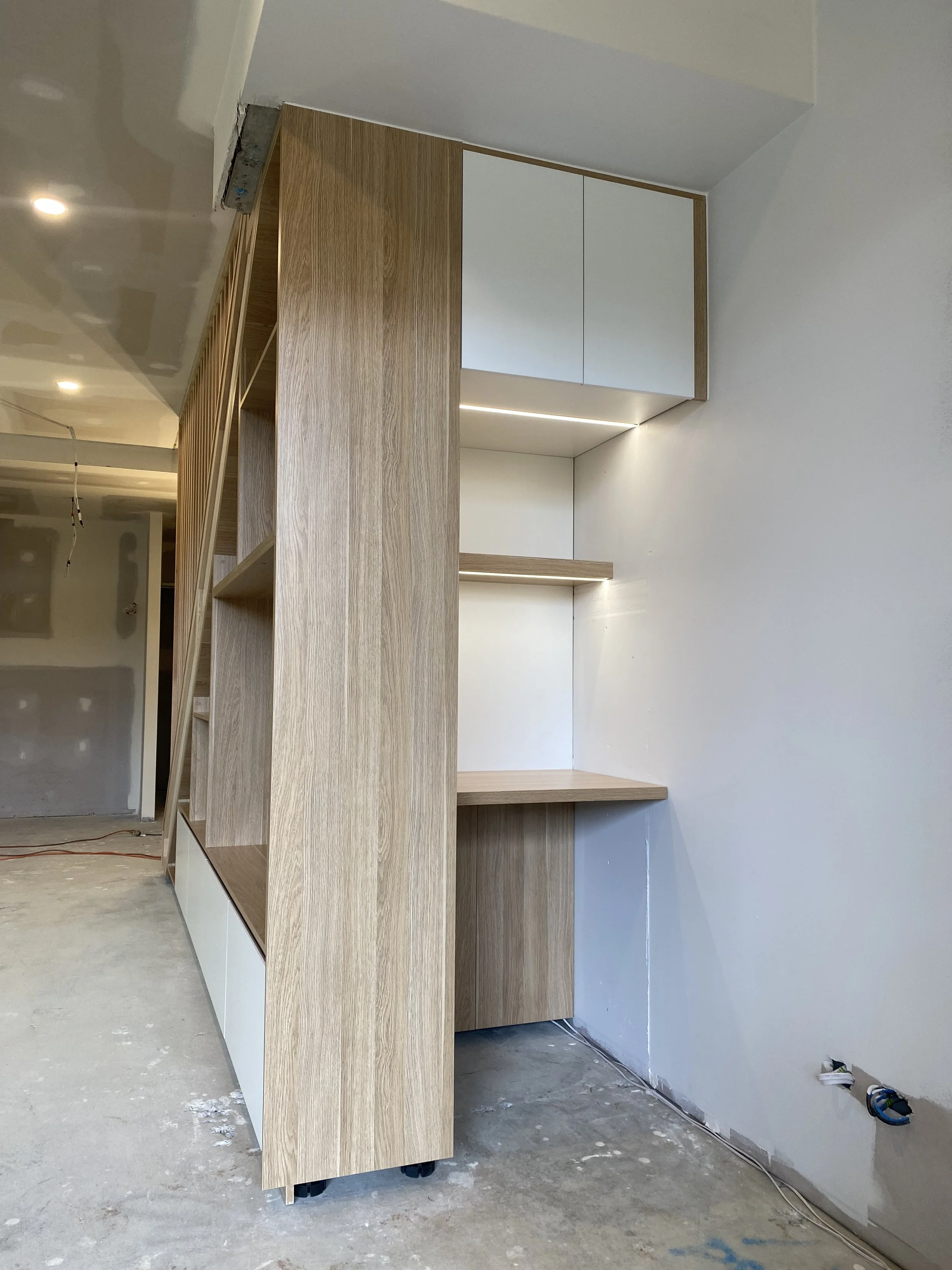 Custom under stairs cabinetry with timber panels, open shelving, and built-in desk during installation