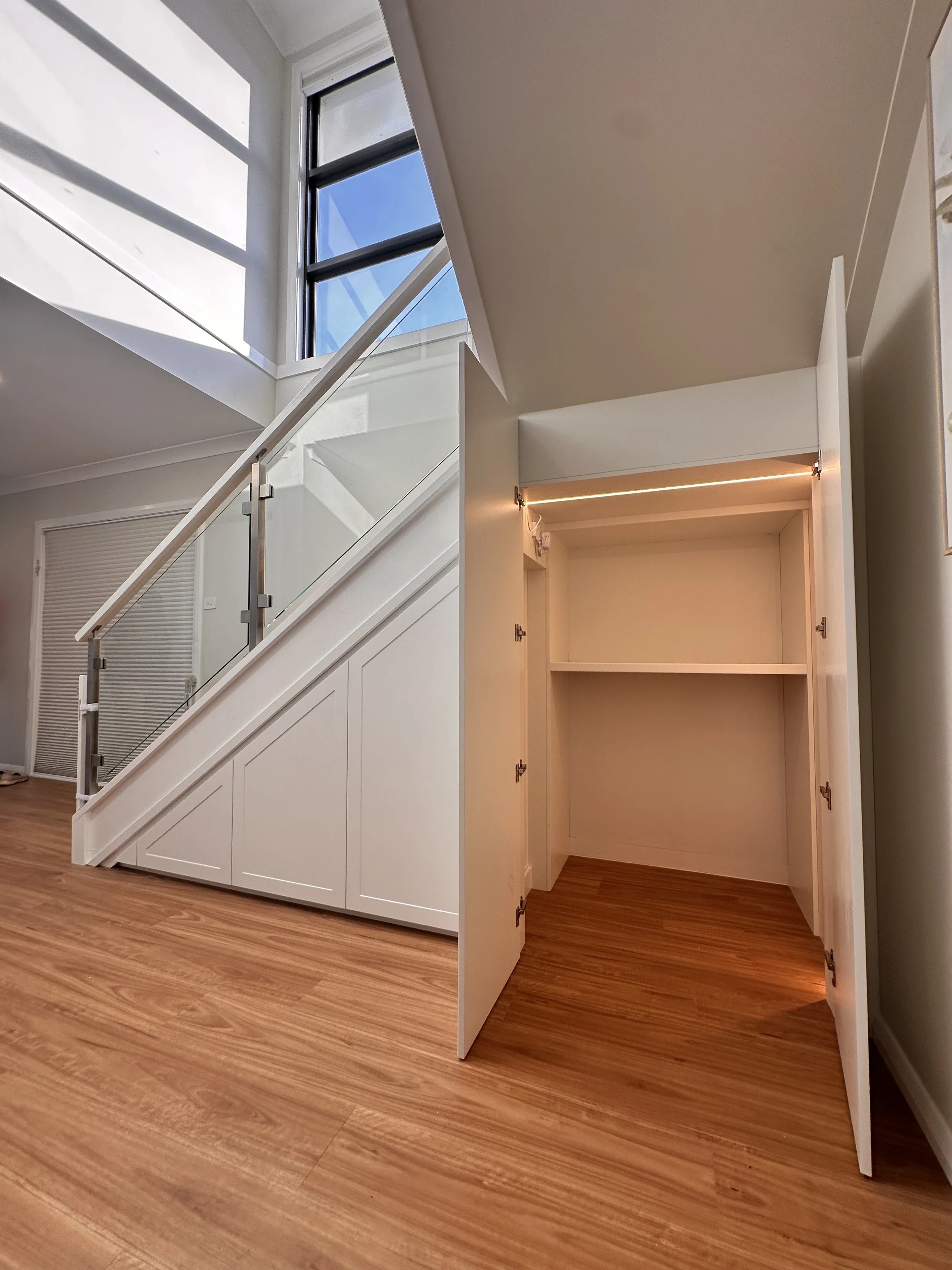 Custom staircase storage with LED-lit cabinetry and shelving inside