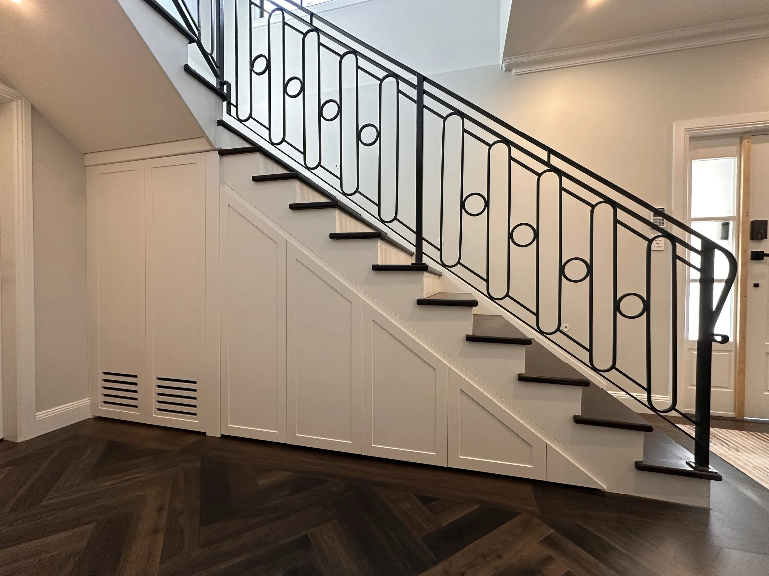 Custom under stairs cabinetry in white polyurethane with drawers and storage.