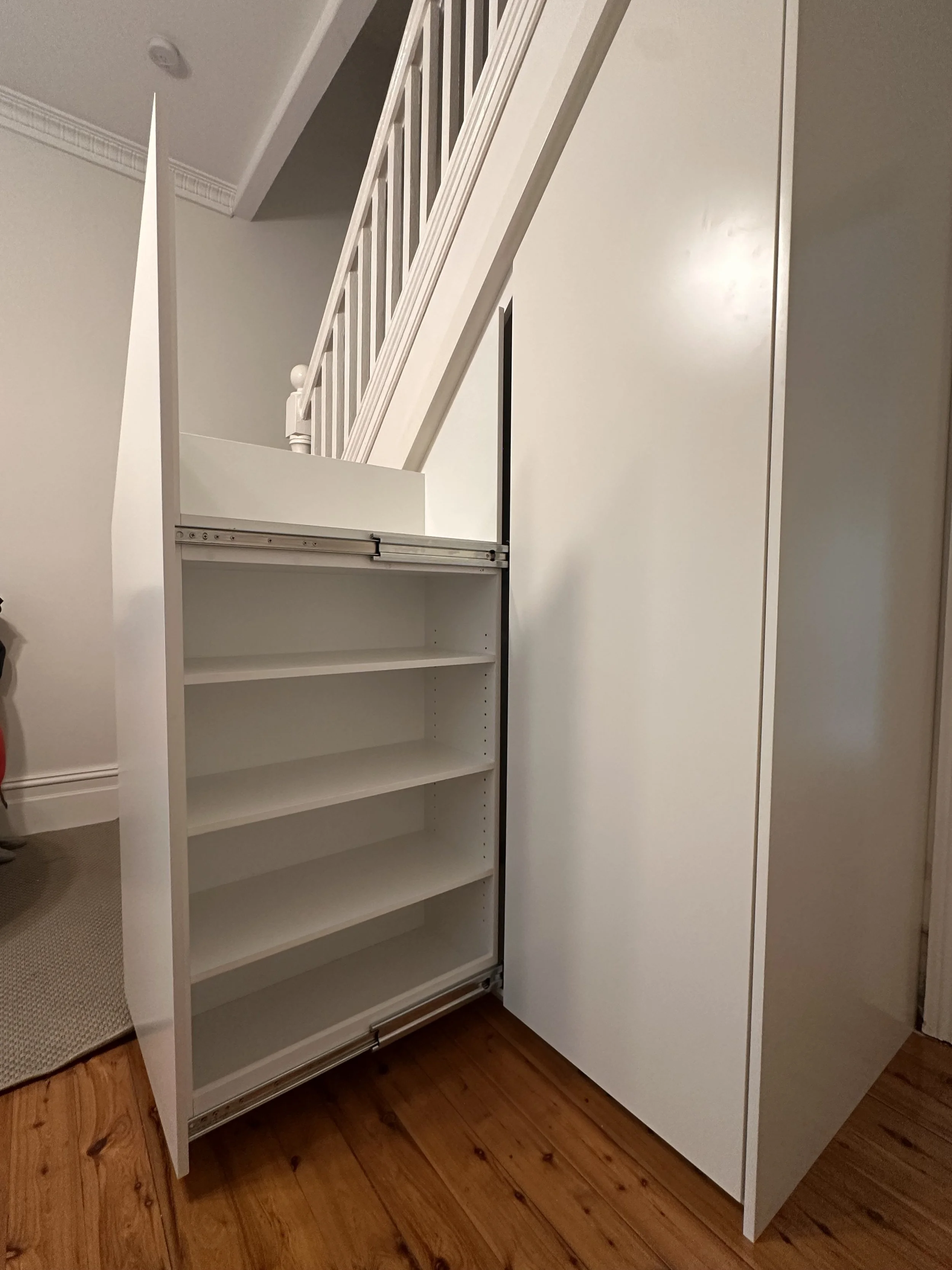 Custom under stairs cabinetry in white polyurethane with heavy duty pull-out drawers
